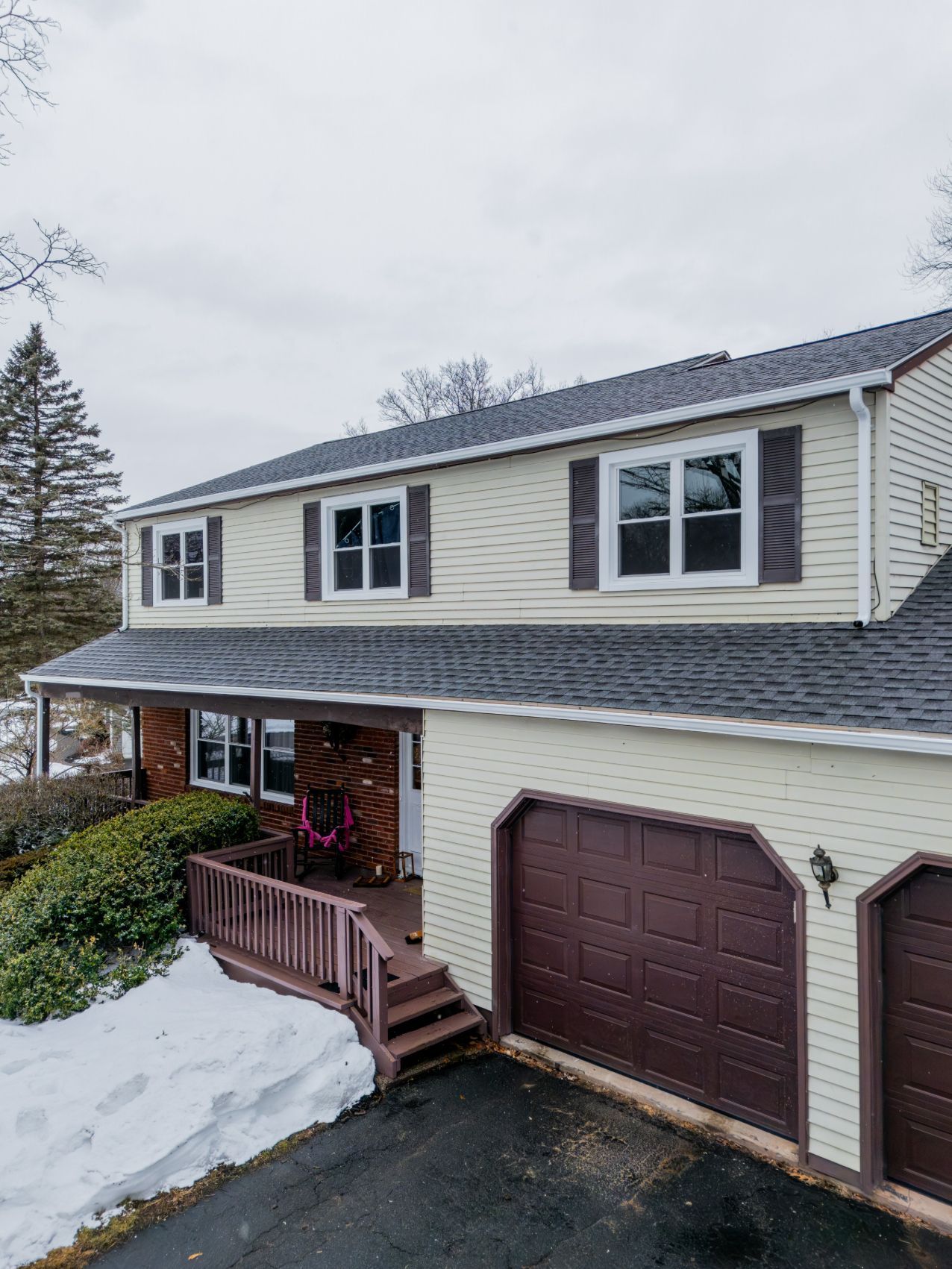 Snow-covered suburban house with white siding, brown garage door, and a front porch in winter.