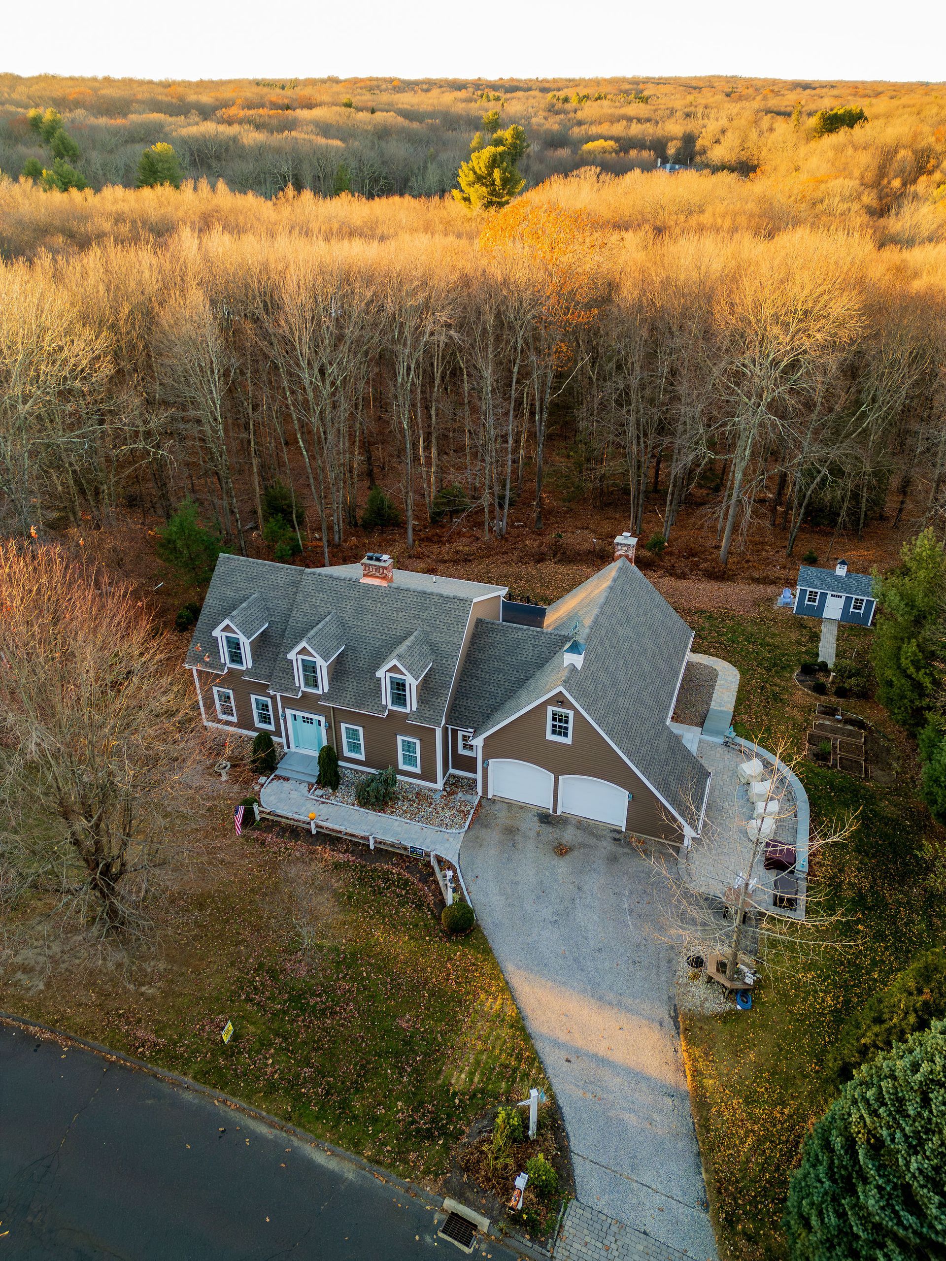 Brown house with a long driveway nestled among fall foliage.