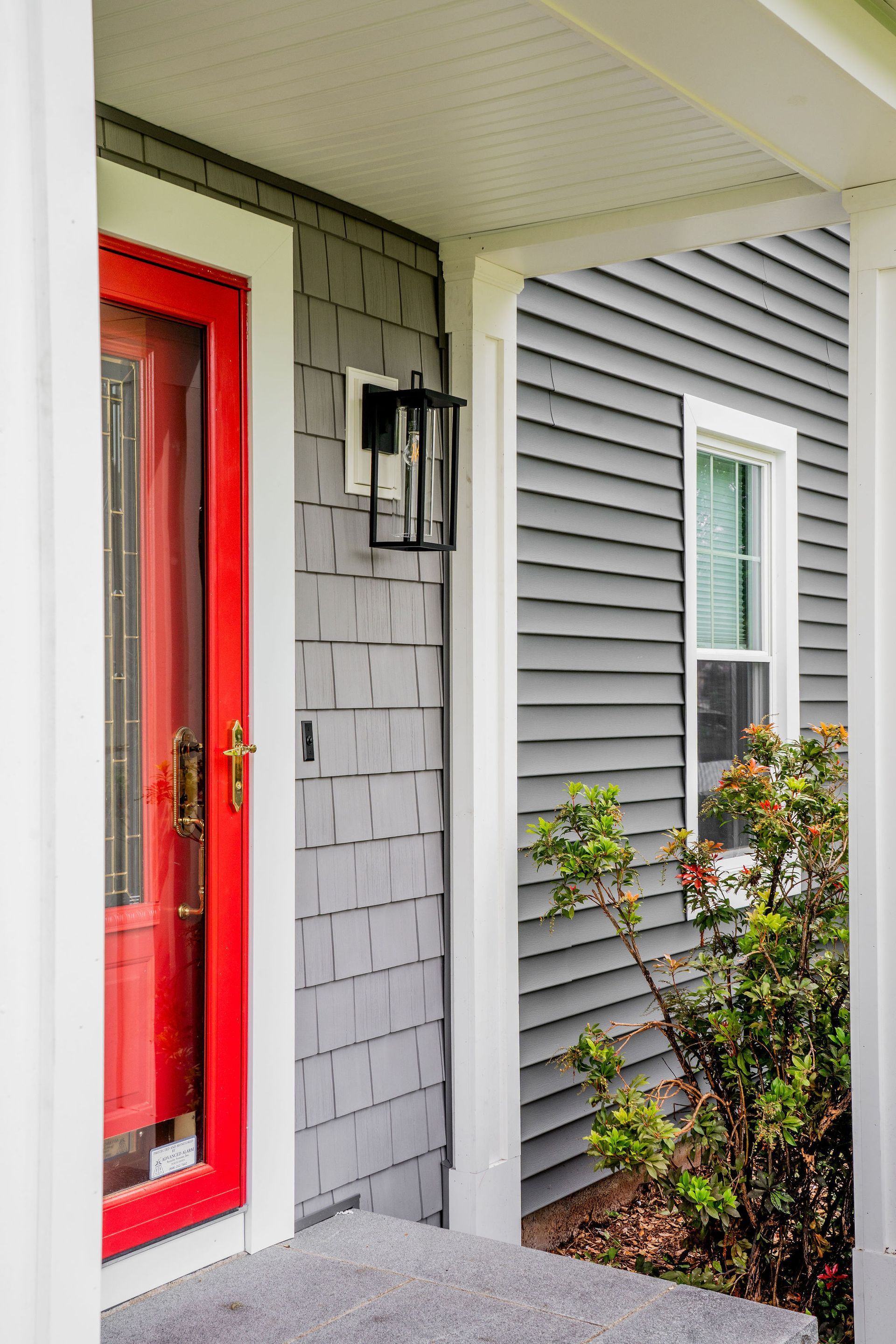 Red door with white trim, gray siding, porch light, and window.