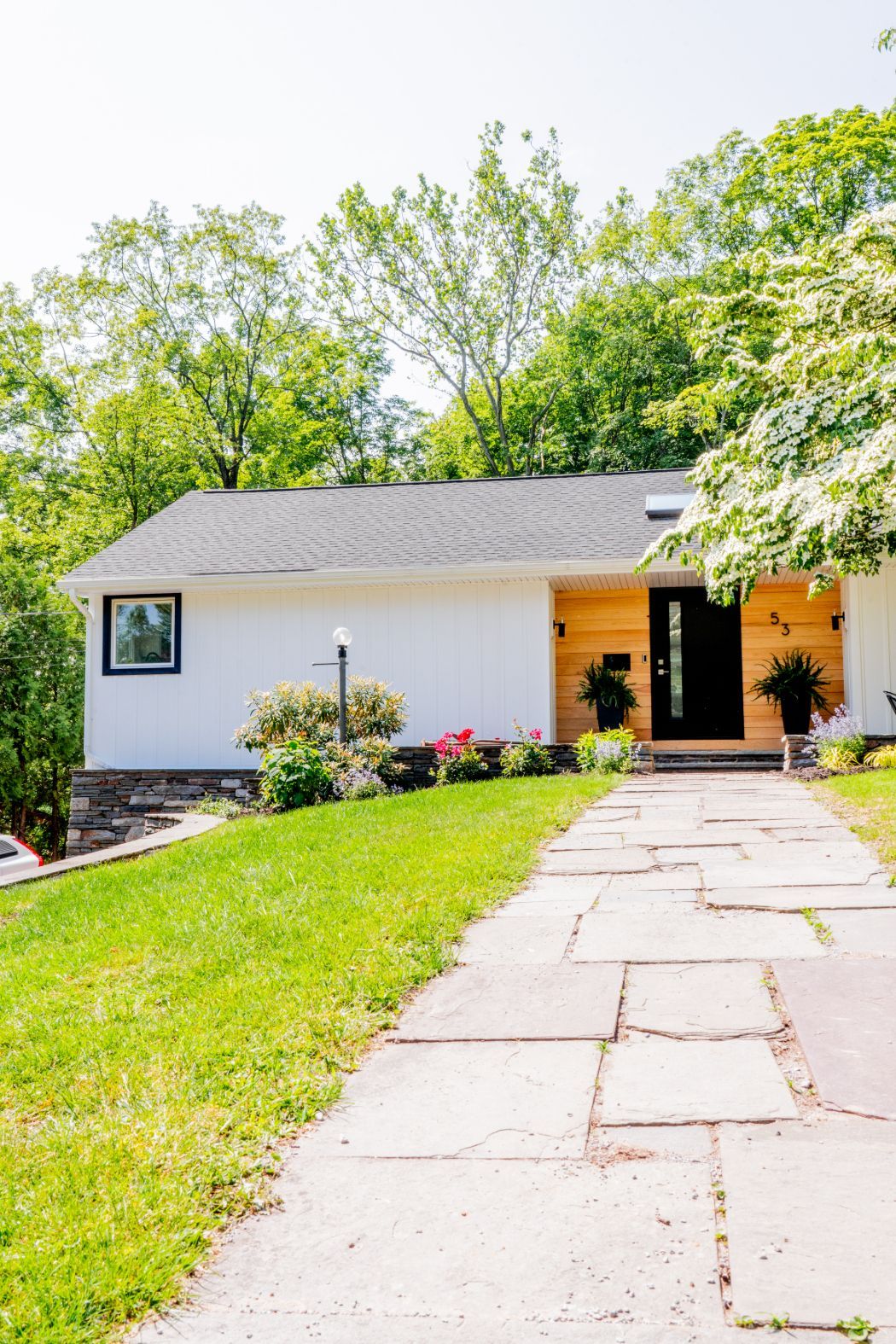 Suburban house with white siding, a stone walkway, and a green lawn shaded by trees.