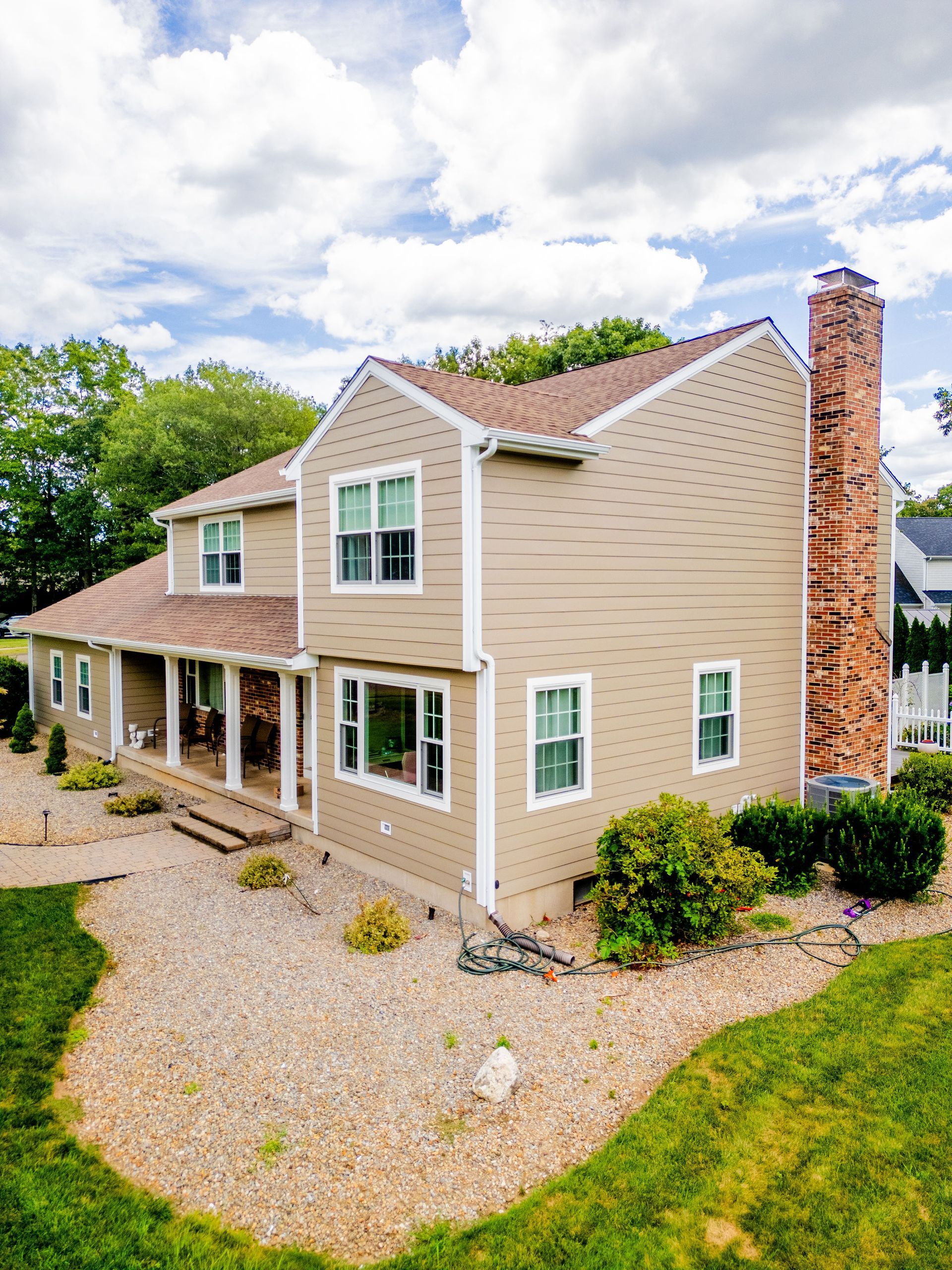 Two-story beige house with a brick chimney under a cloudy sky.