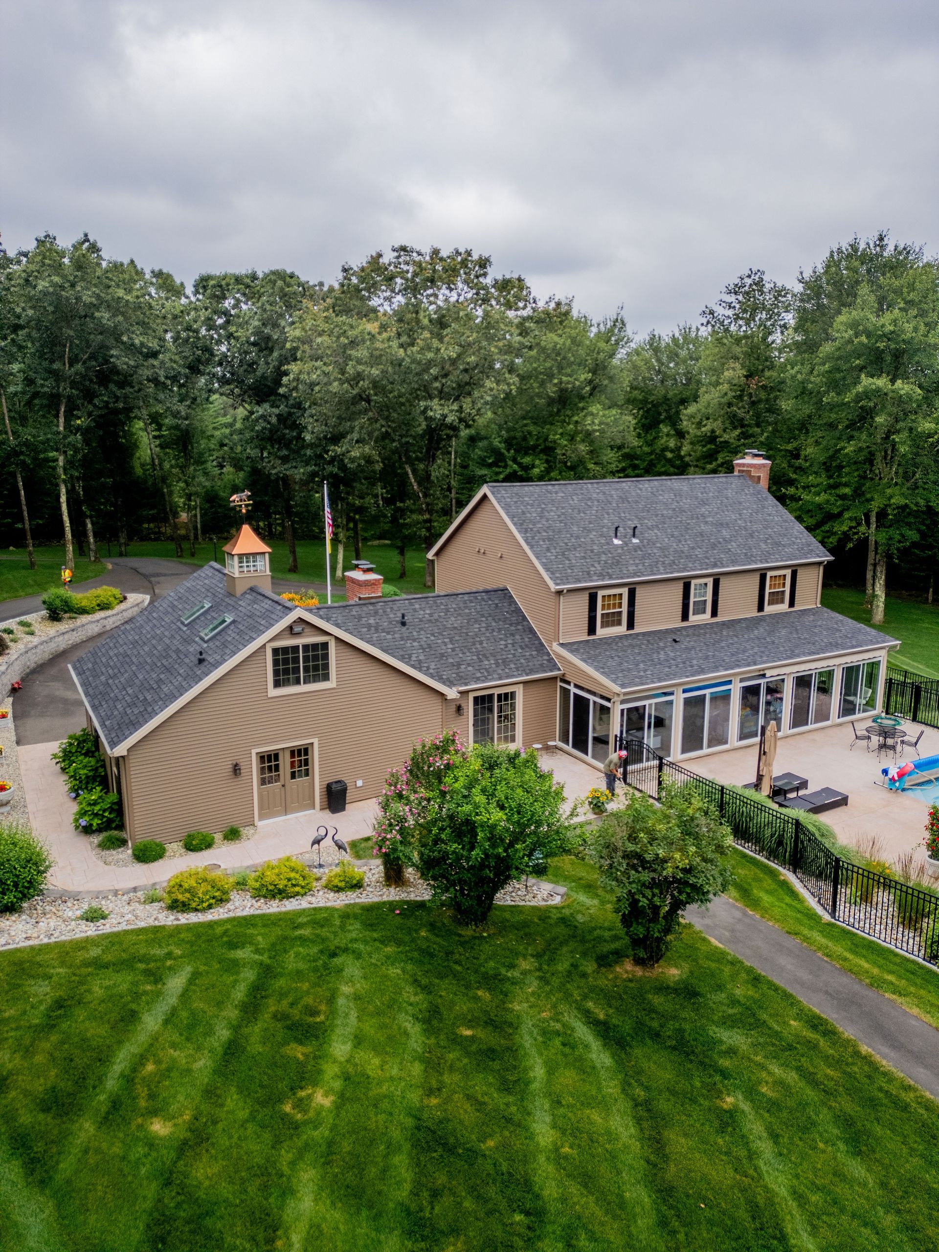 Aerial view of a large, brown house with a pool, surrounded by trees and a green lawn.