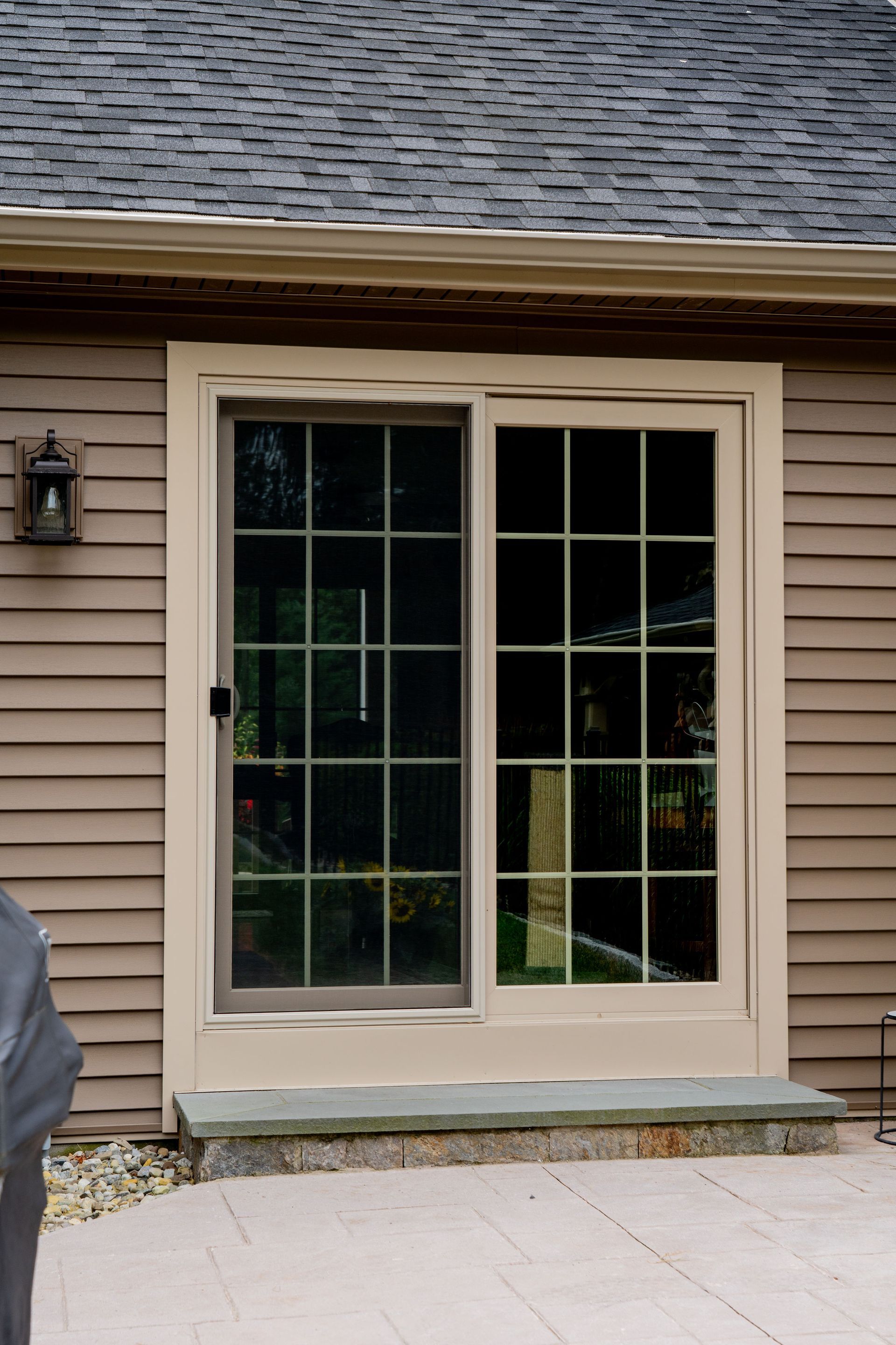 Sliding glass door with grid pattern panes set in a tan frame on a brown house with a gray roof.
