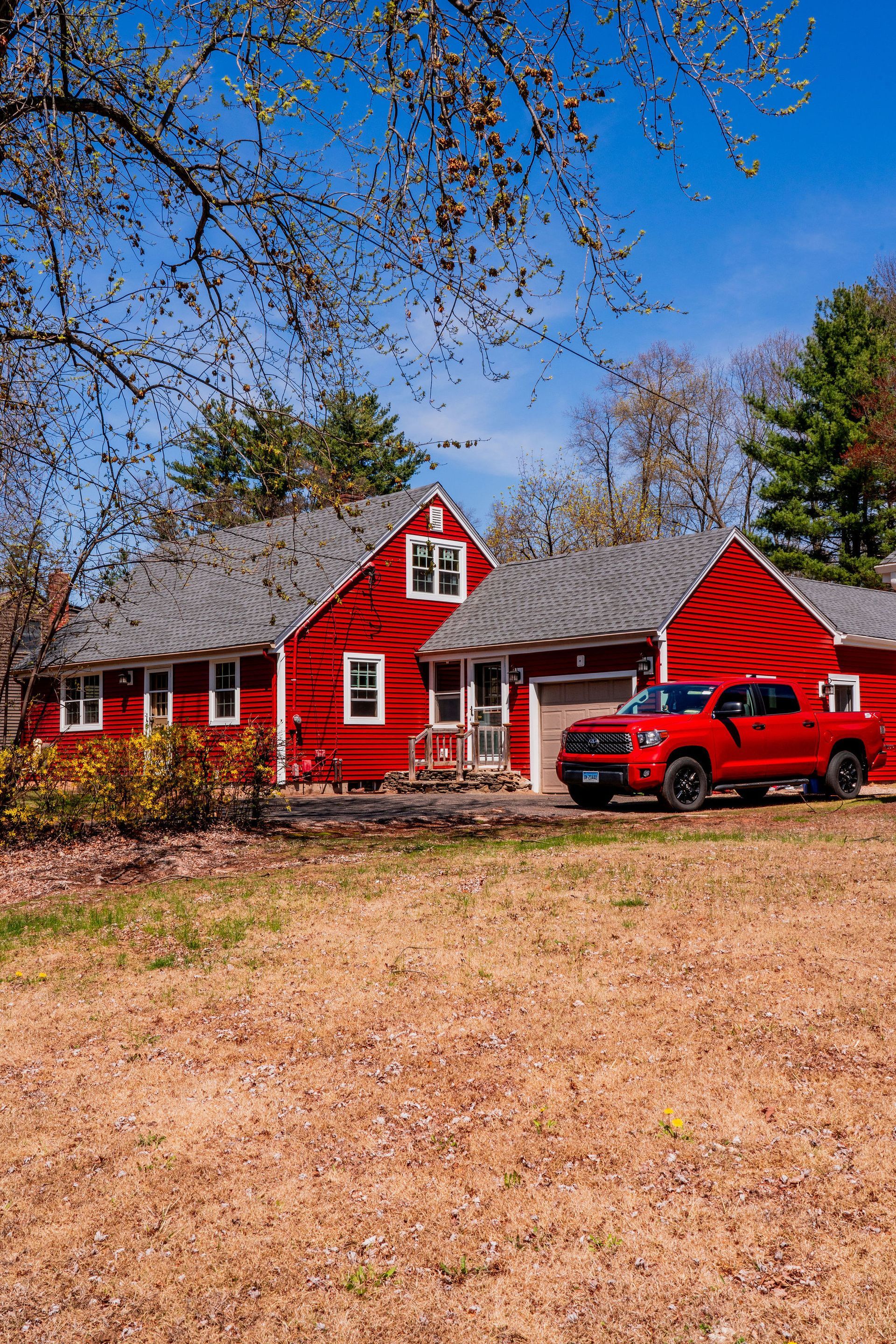 Red house with a red truck parked in front, under a blue sky.
