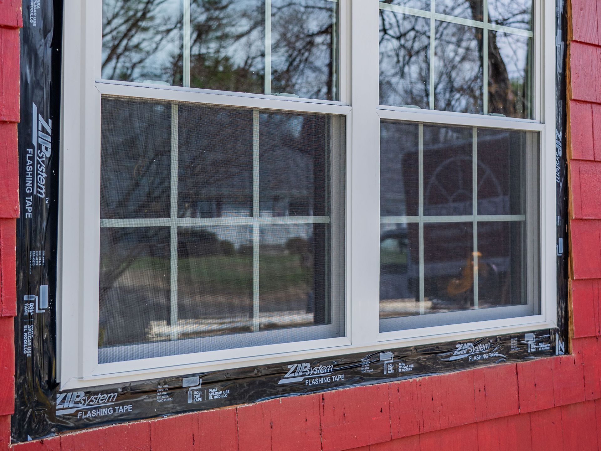 A vinyl window being installed on a red house.