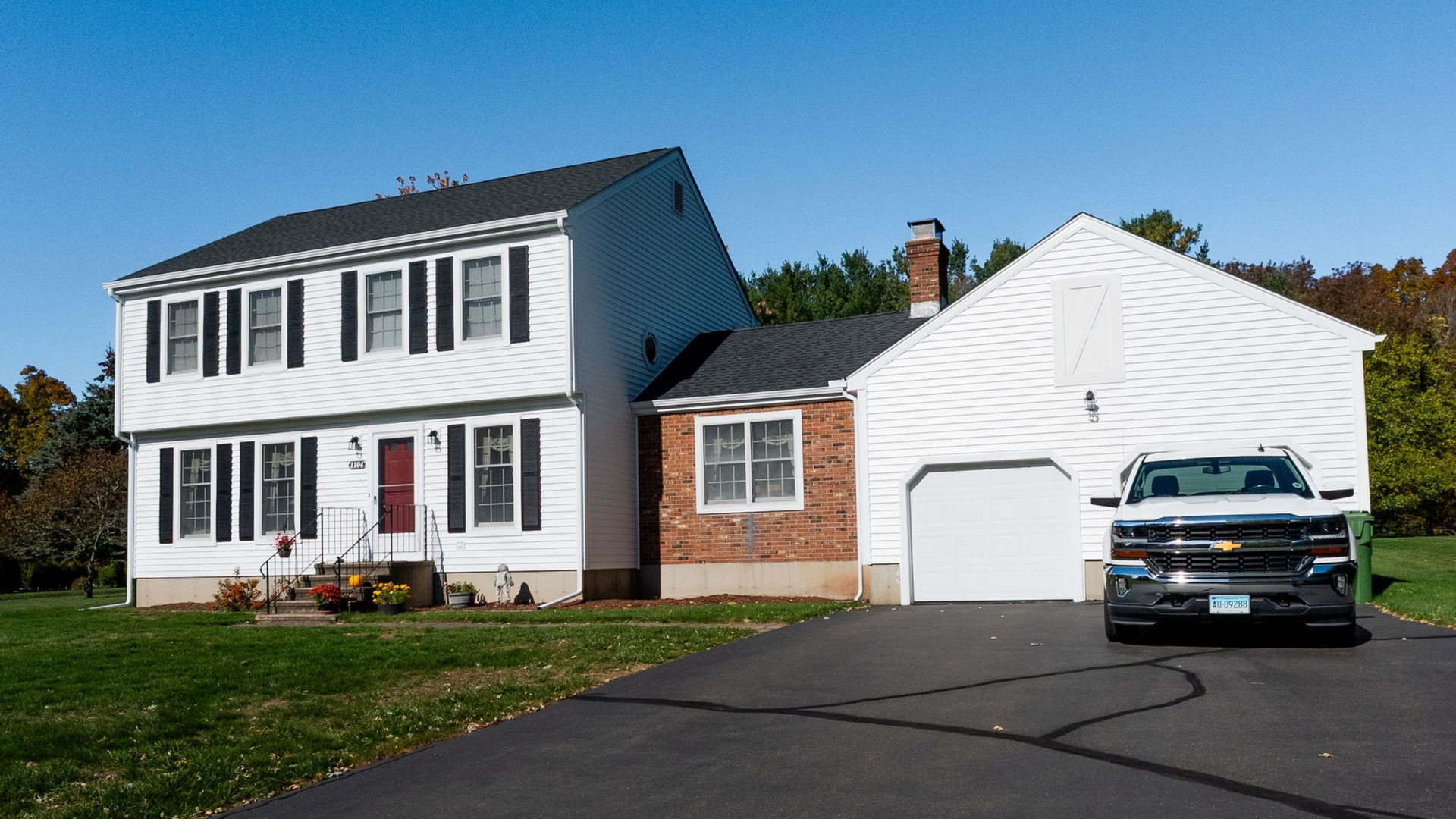 Two-story white house with black shutters, attached garage, and a pickup truck parked in the driveway.
