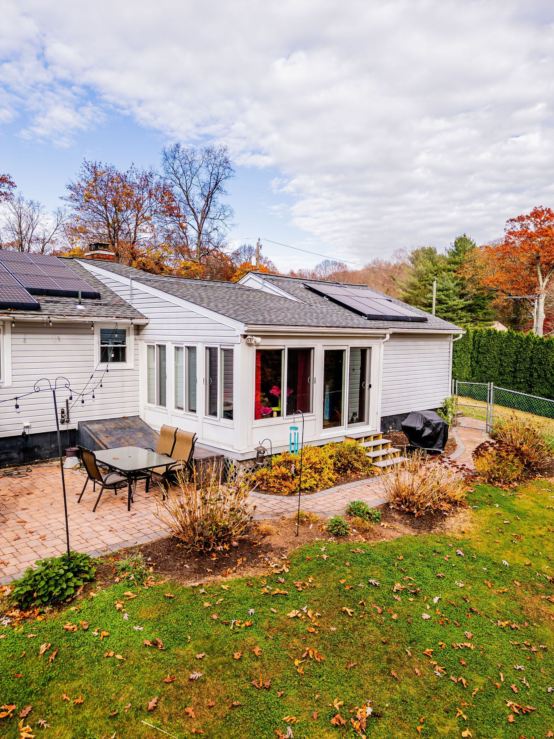 Backyard with white house, sunroom, solar panels, and fall foliage.