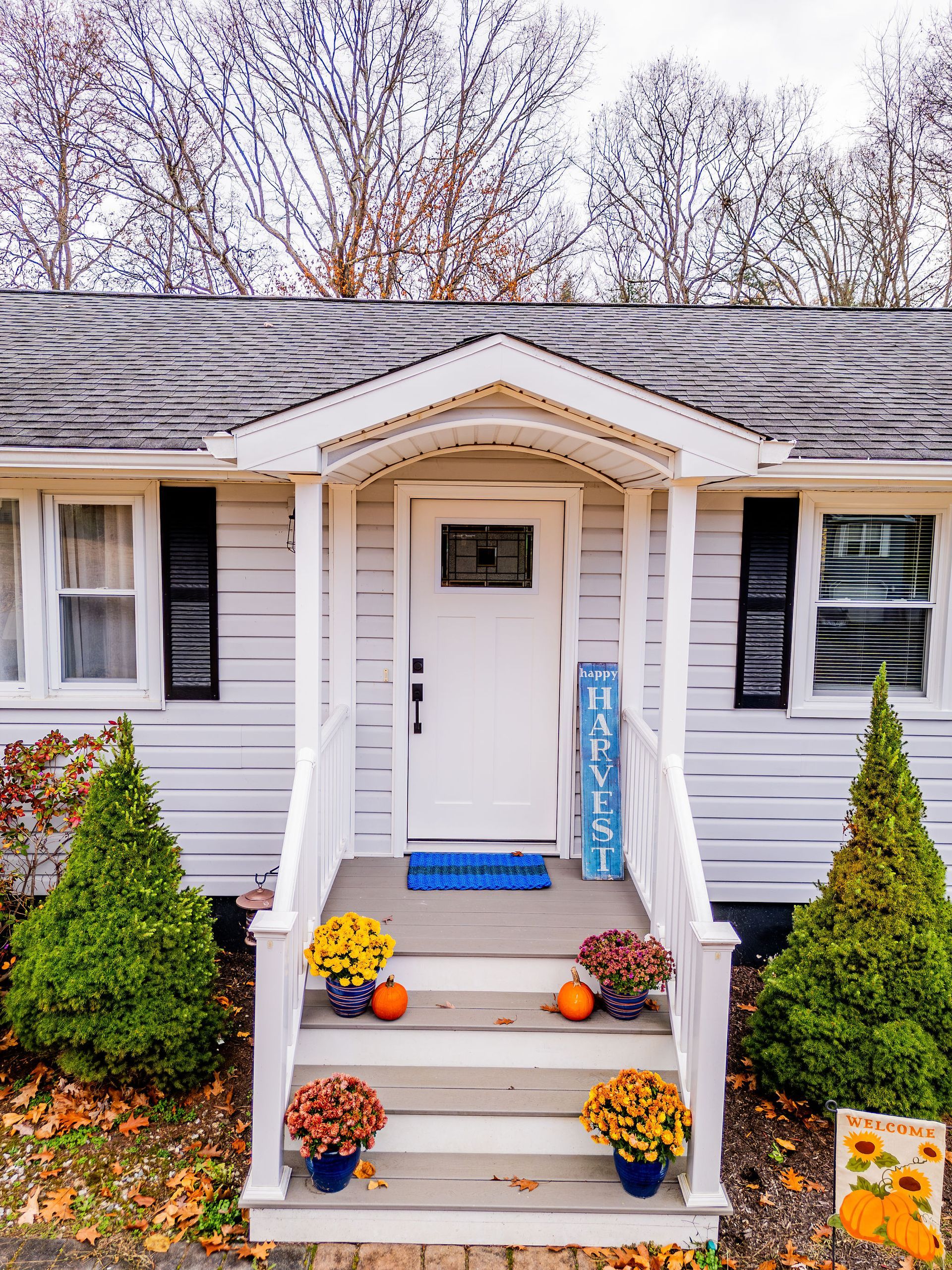 White house with porch decorated for fall: pumpkins, mums, and a 