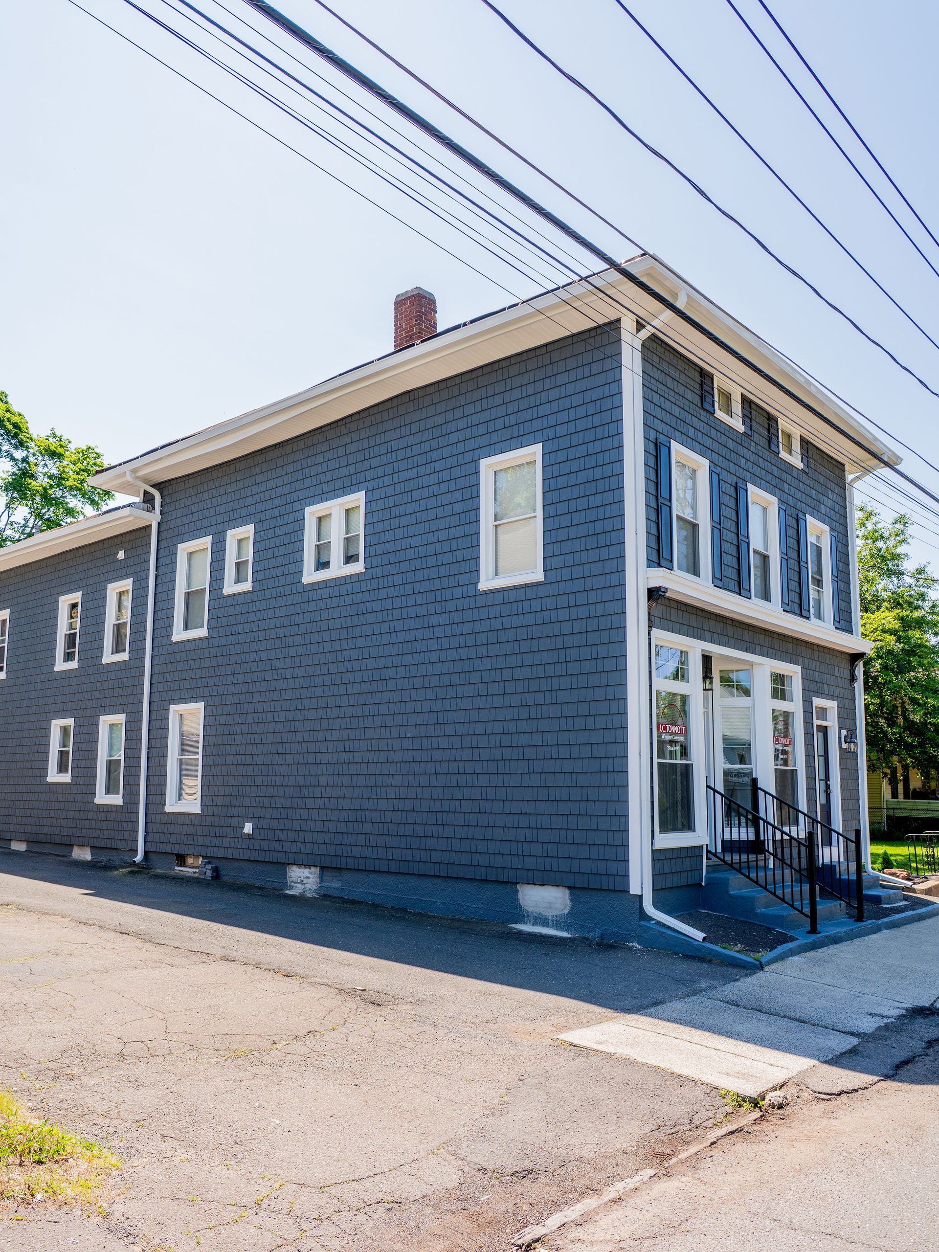 Two-story blue house with white trim and windows on a slight incline.