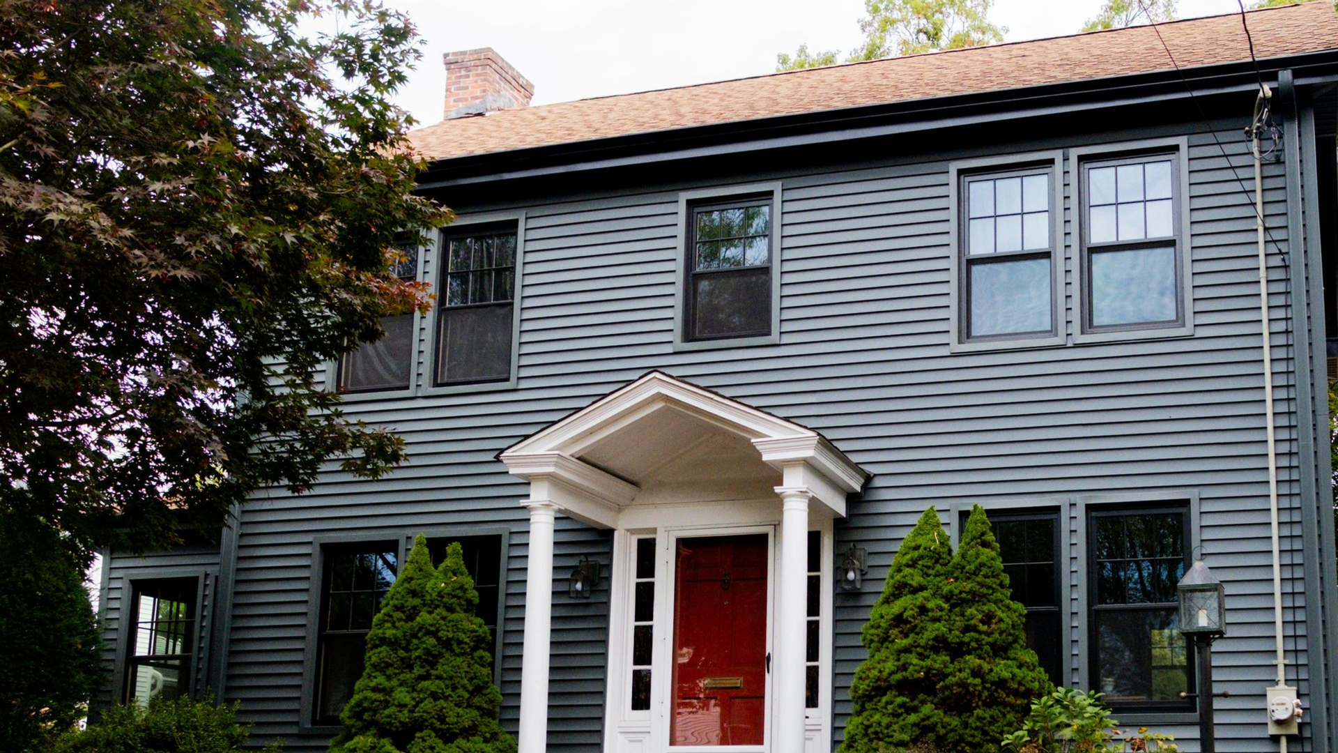 Gray two-story house with a red door, white trim, and a small porch.