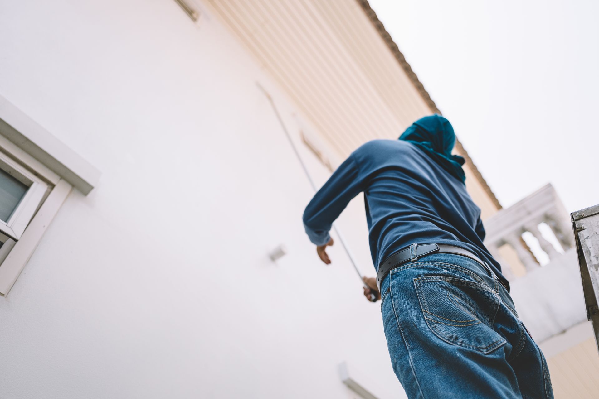 Person in blue climbing or reaching up beside a white building, viewed from below