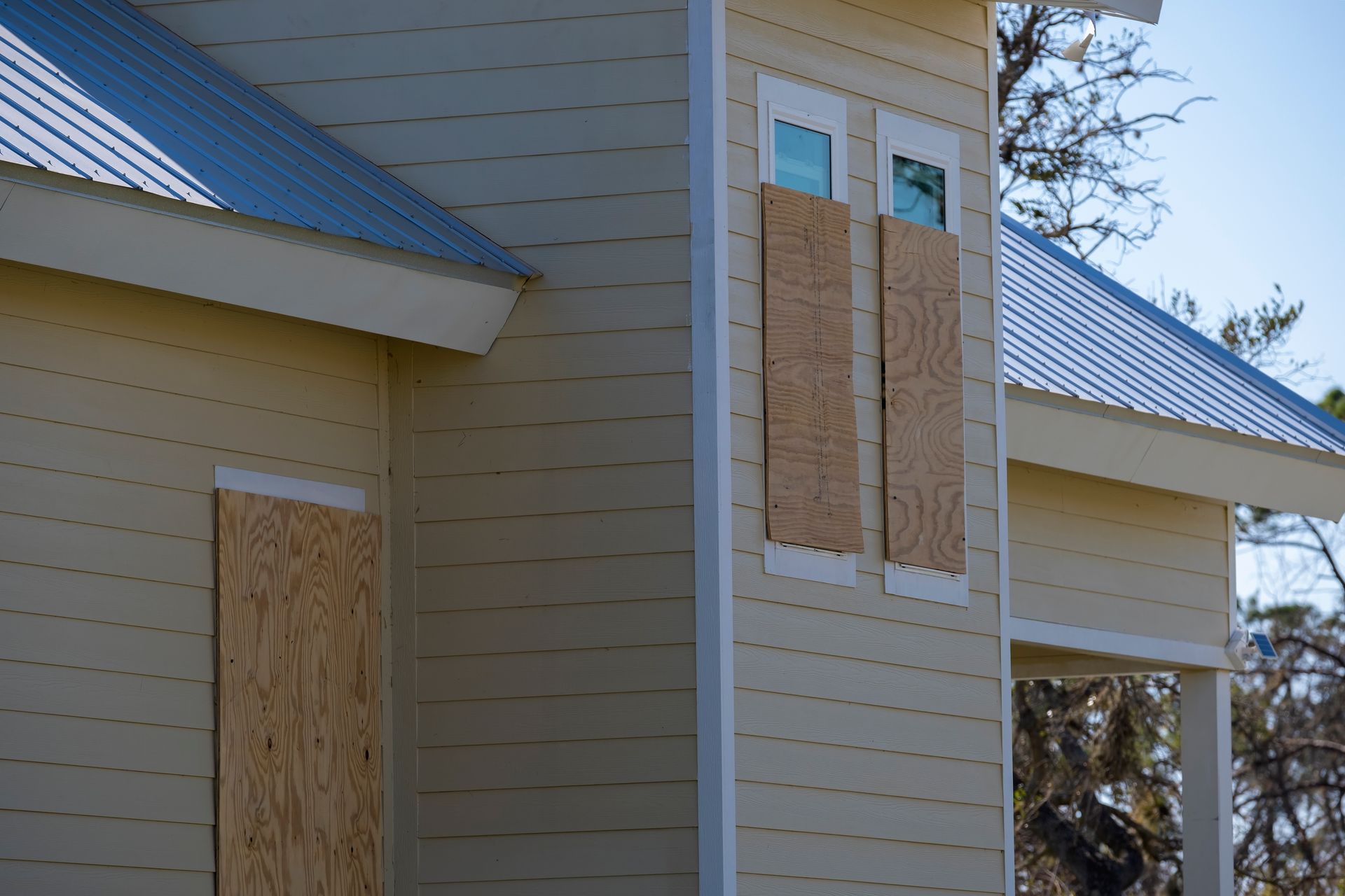 House exterior with boarded-up windows and white siding under a blue roof