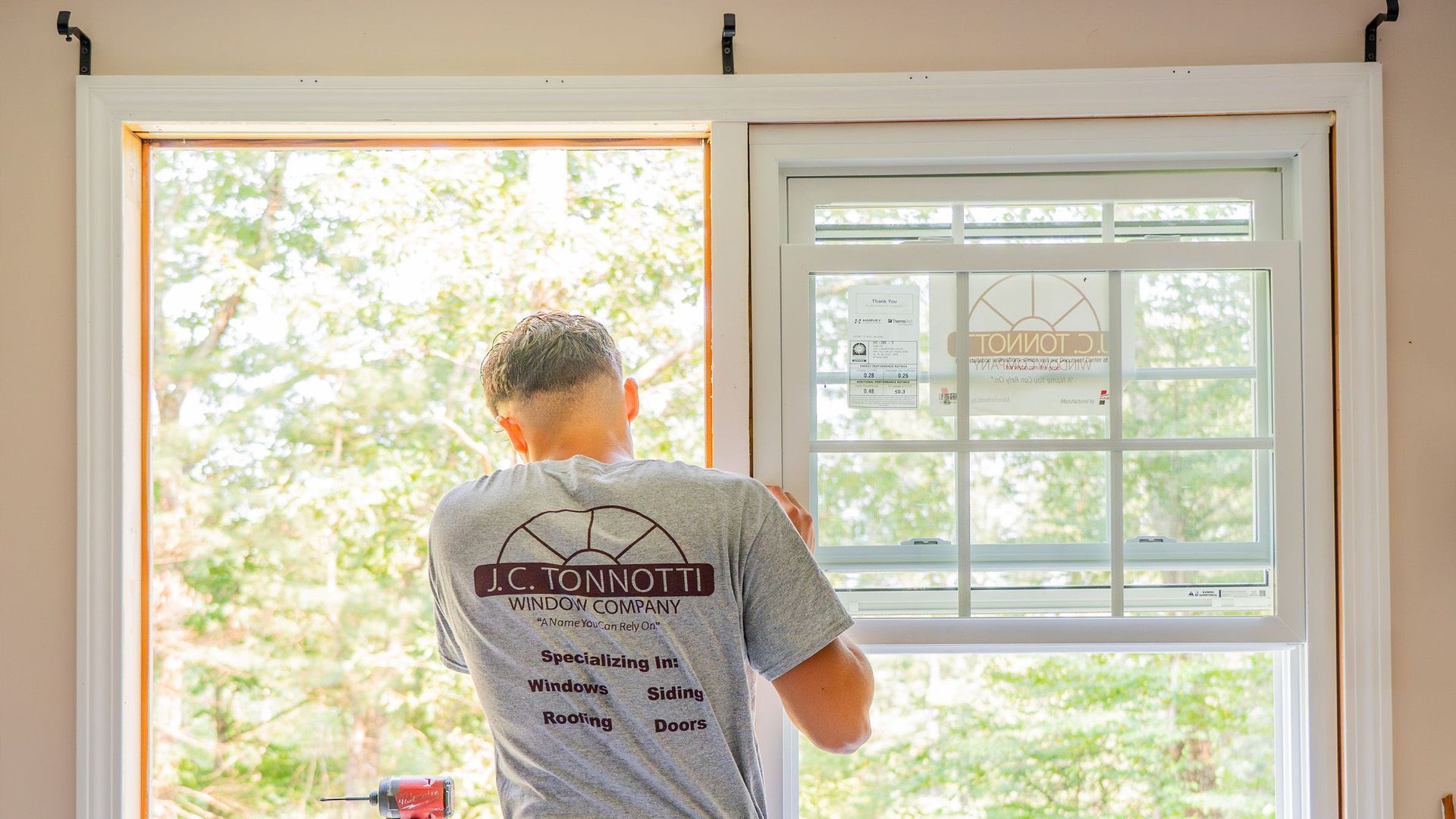 A person installing a new window indoors, with trees visible outside.