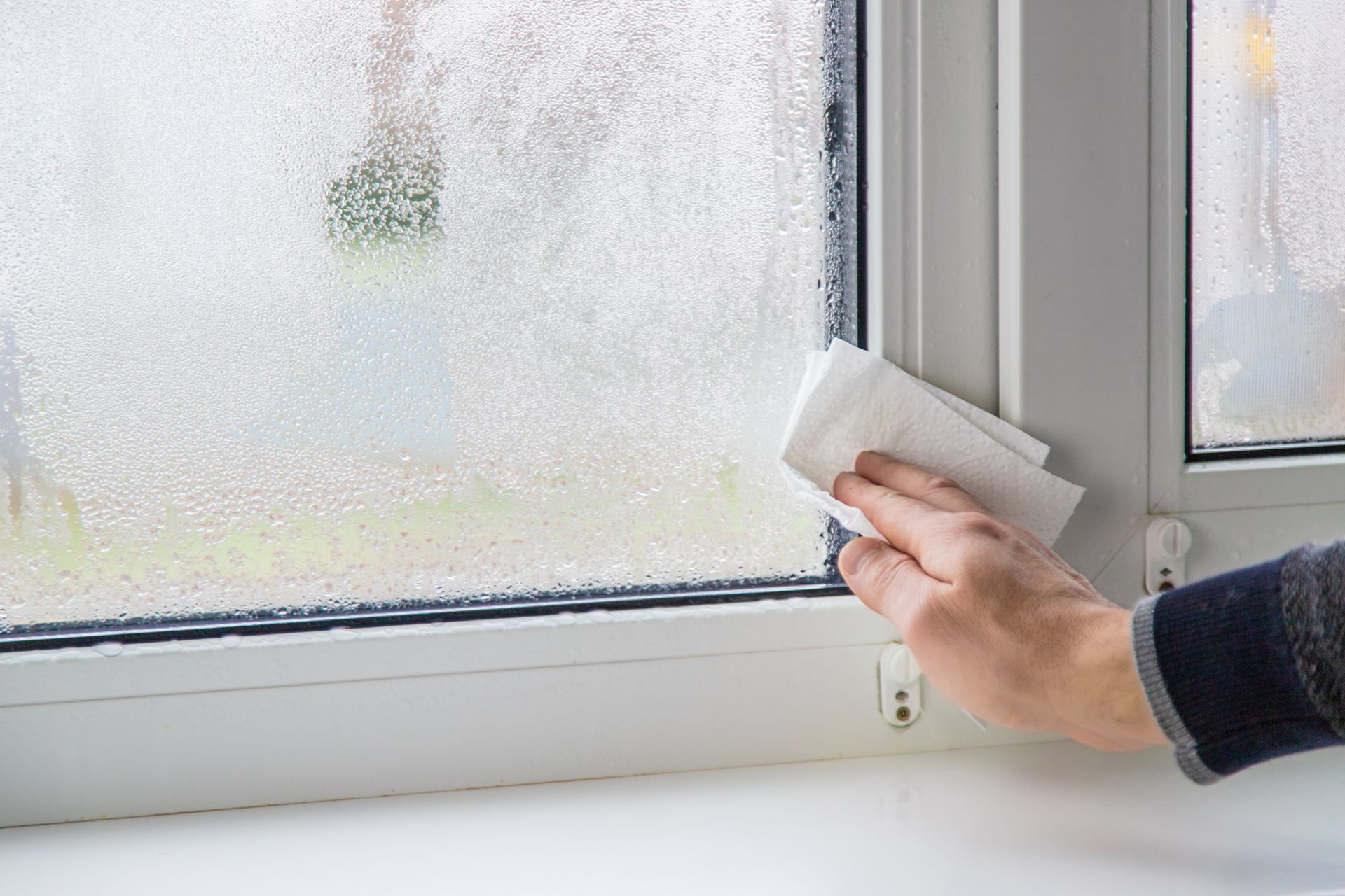 Hand cleaning a fogged window with a white cloth from inside a room