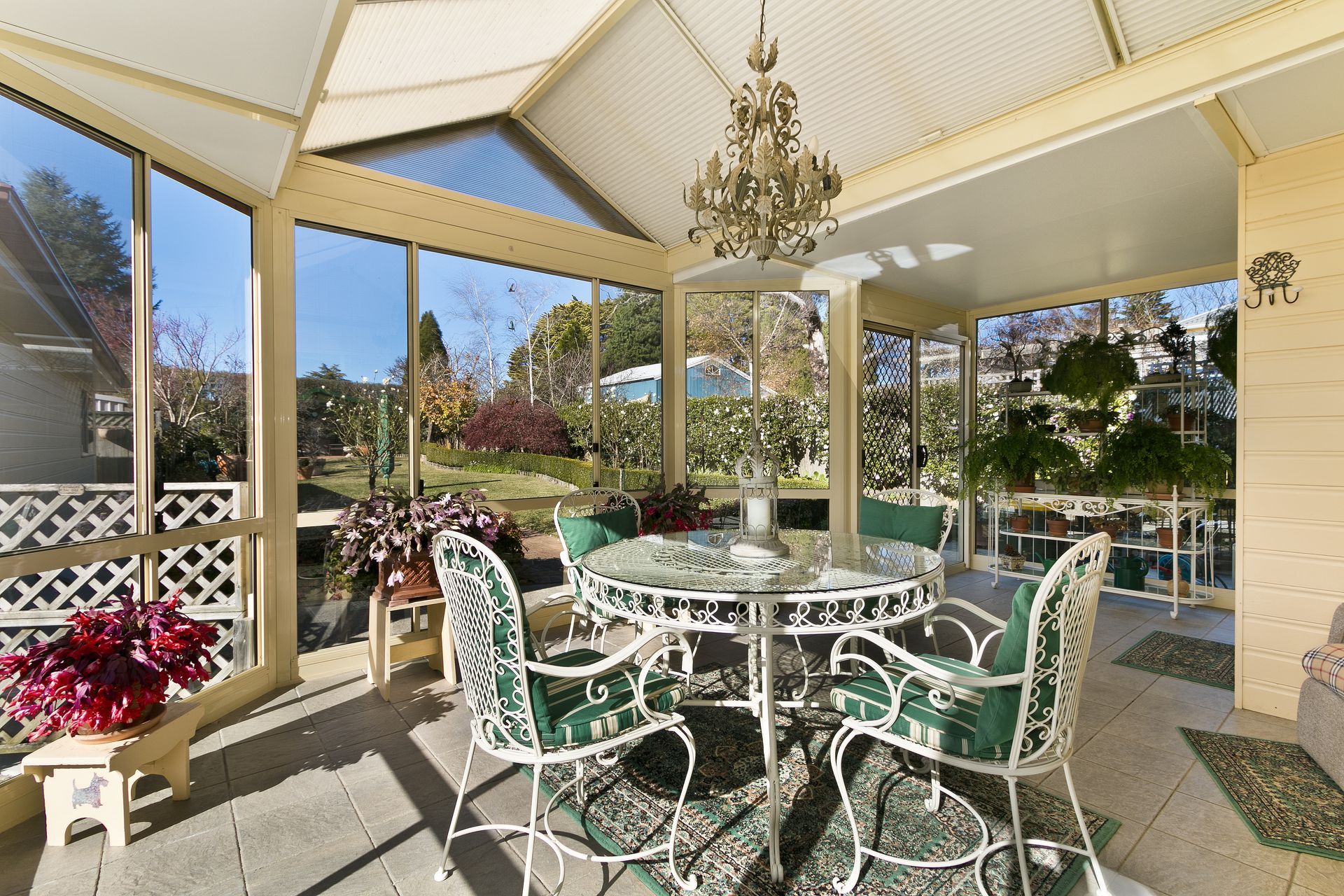 Sunlit gazebo with white wrought-iron patio table and chairs overlooking a garden.