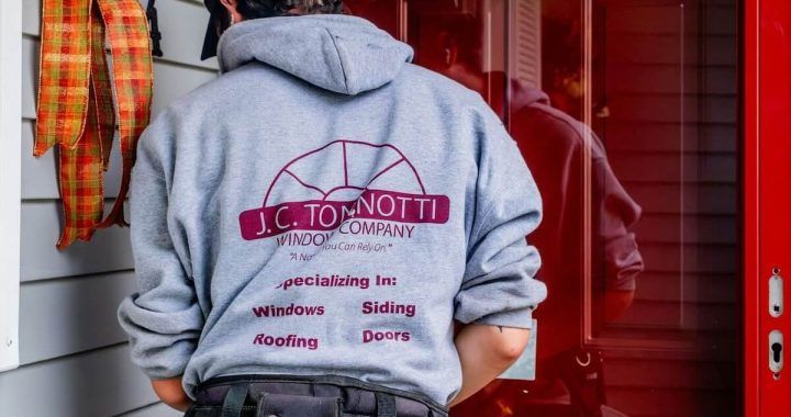 A man wearing a hoodie that says jc tonnotti is standing in front of a red door.