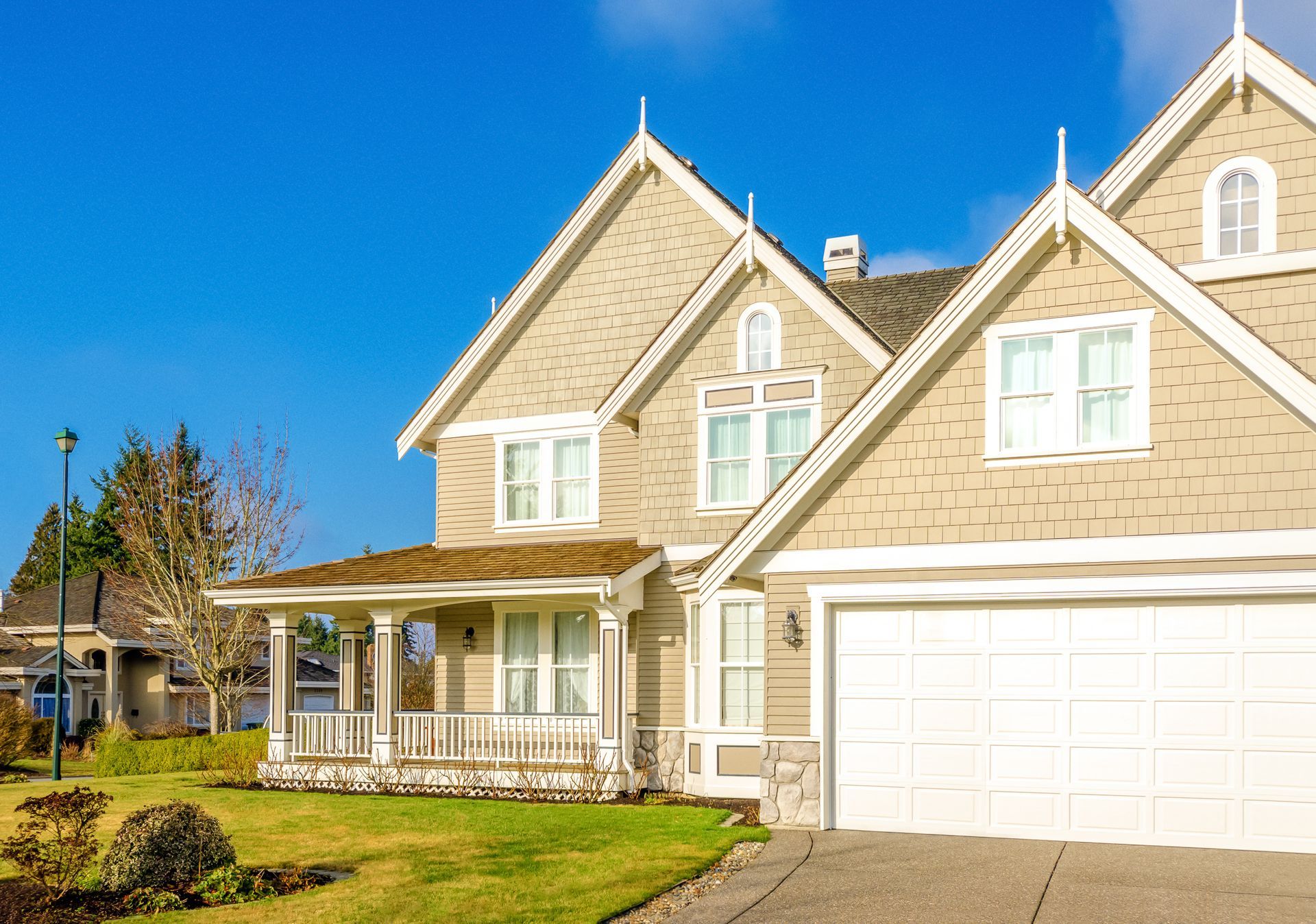 Suburban beige house with white trim, front porch, and two-car garage on a sunny day