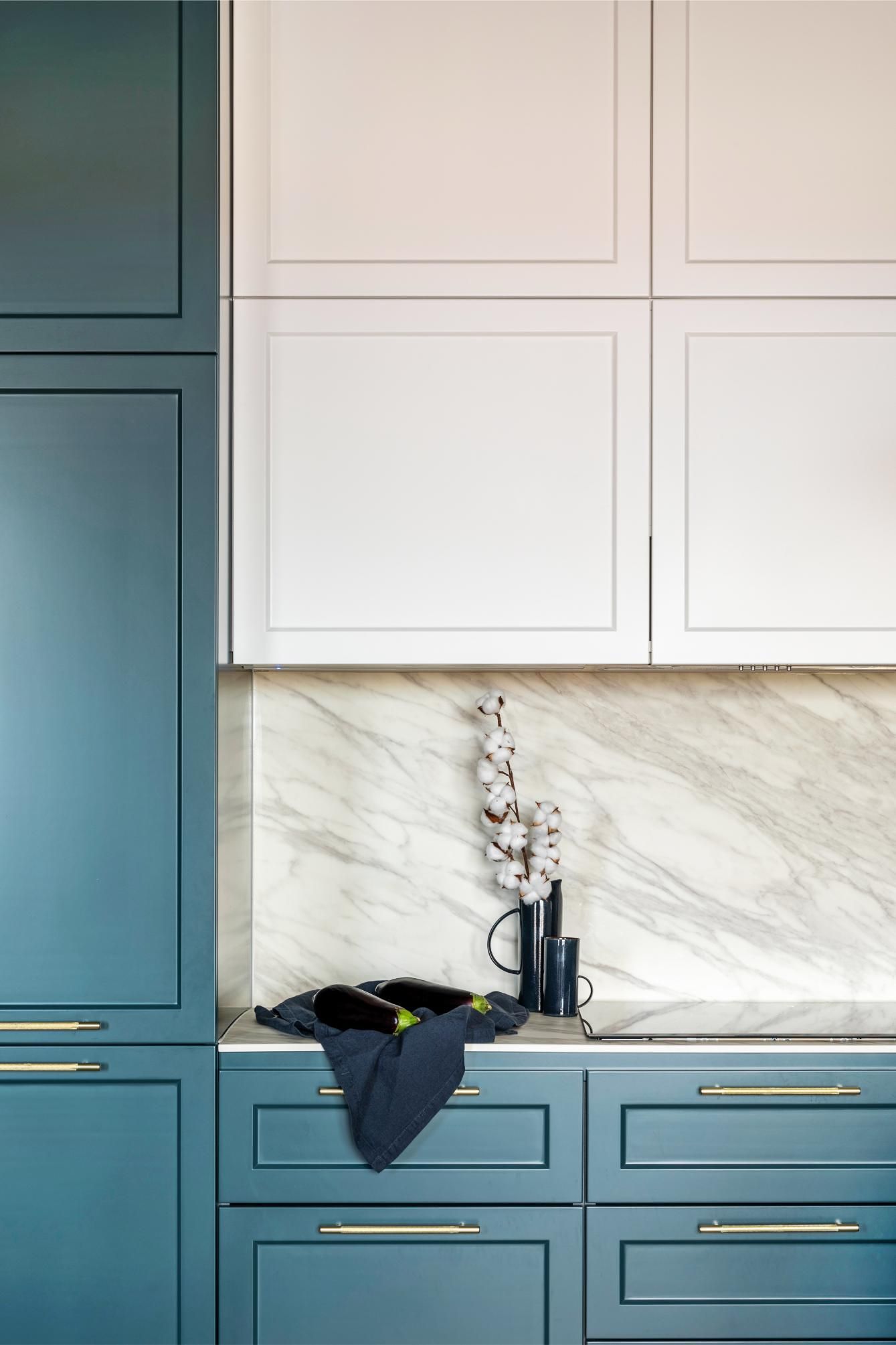 Blue and white kitchen cabinets with marble backsplash and decorative flowers.