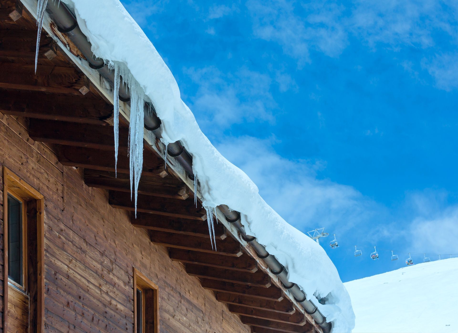 Snow and icicles on a wooden roof against a bright blue sky.