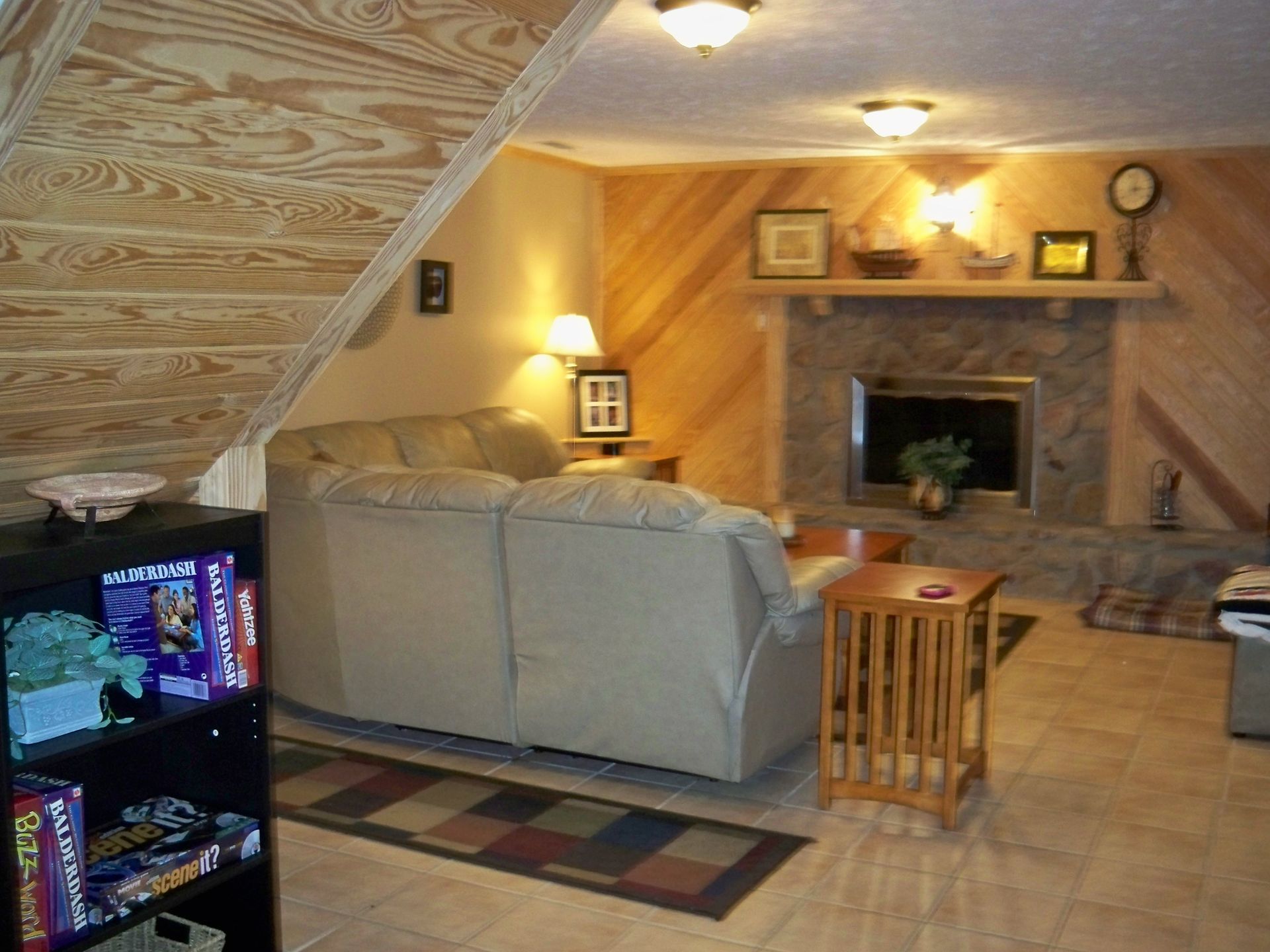 Cozy living room with fireplace, beige couch, wood paneling, and board game shelf.