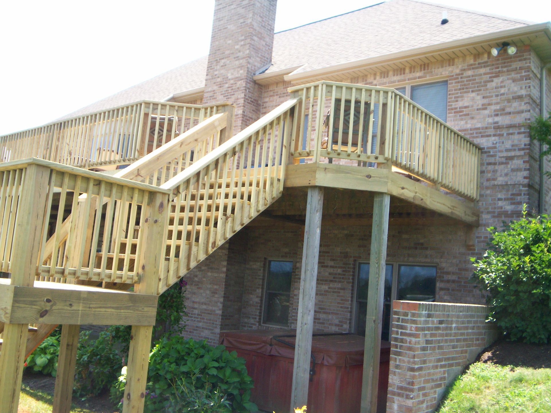 Wooden deck attached to a brick house, featuring stairs, railings, and support posts.