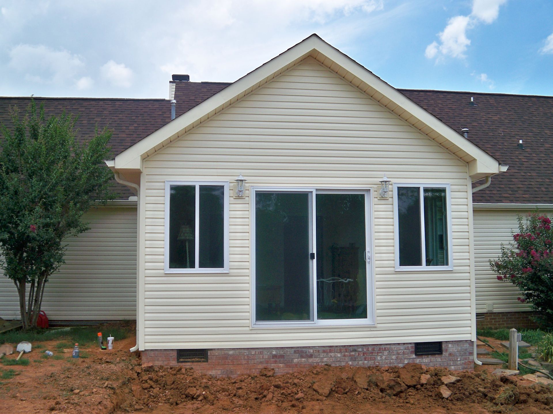 Sunroom addition to a house with beige siding, sliding glass doors, and two windows.