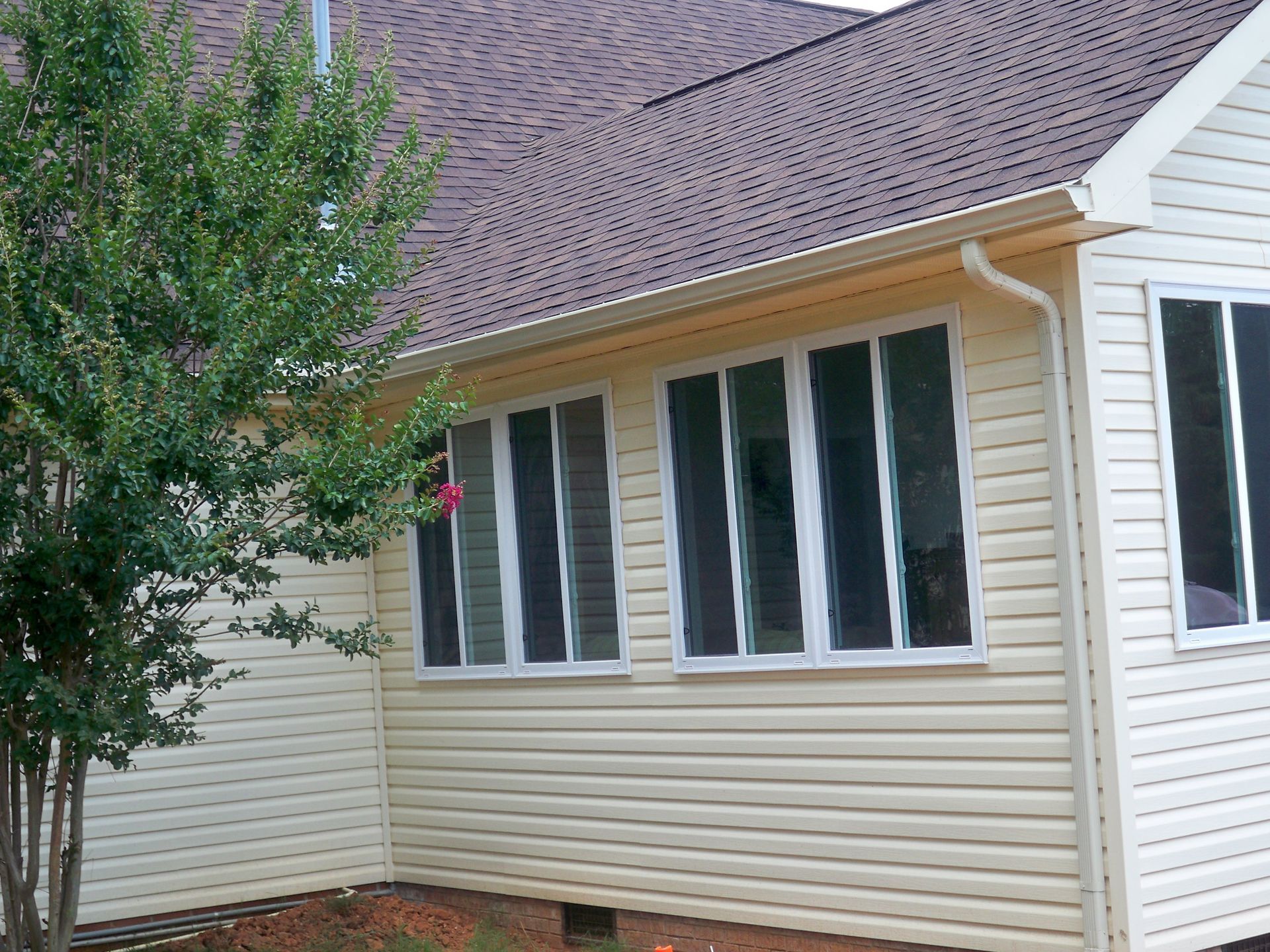 Beige siding and windows on a house with a brown roof; a green tree is on the left.