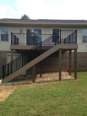Two-story deck with black railings and stairs leading to a back door on a beige house.