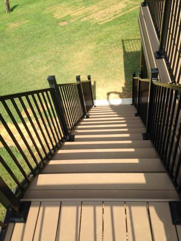 Staircase with brown composite steps and black metal railings leading down to a green lawn.