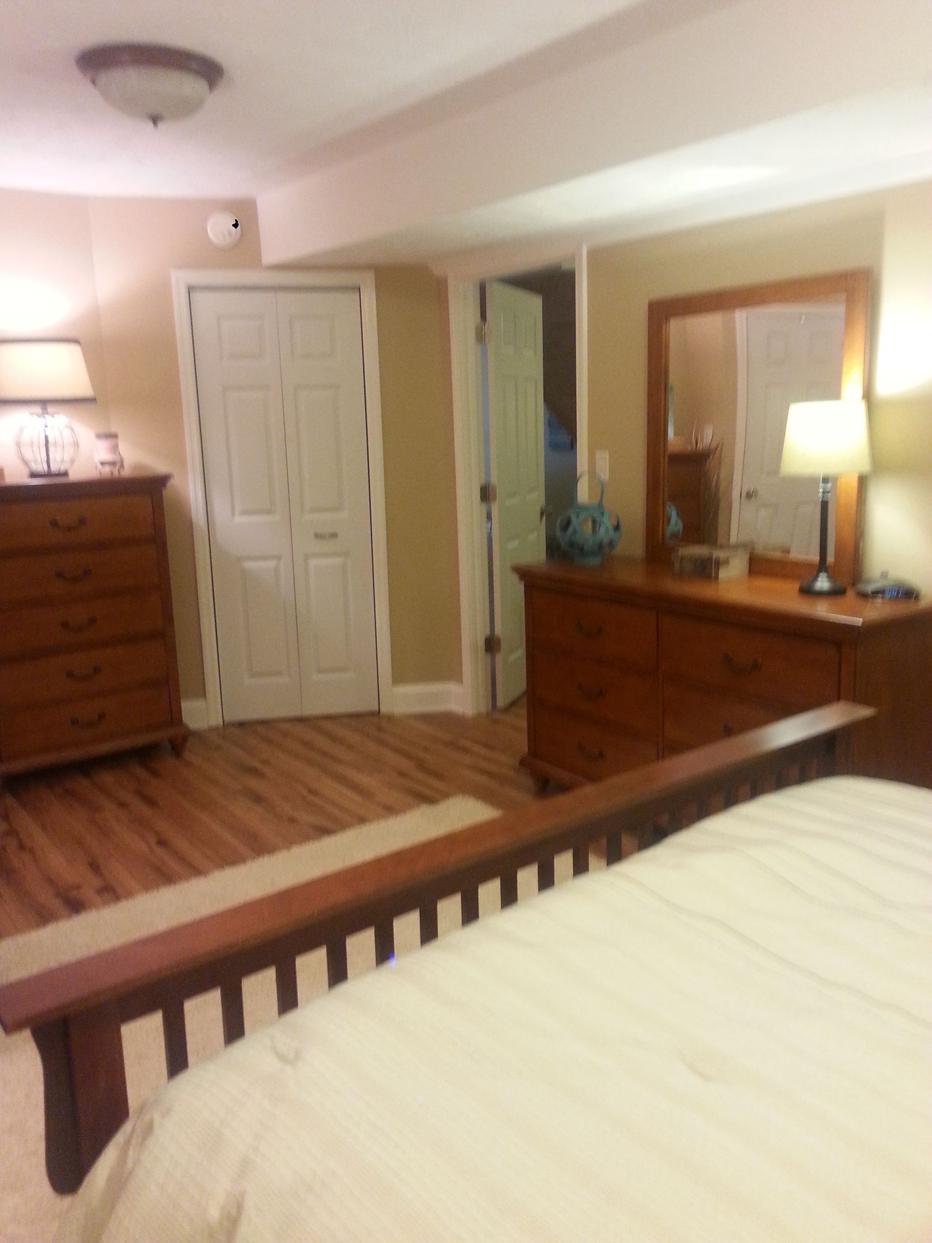 Bedroom with wooden furniture, including a dresser, doors, and a bed. Light beige walls and hardwood floors.