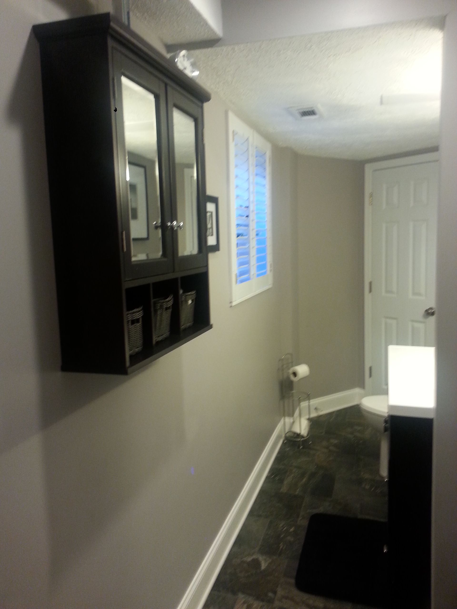 Bathroom with dark vanity, gray walls, and window with shutters. Doorway to toilet visible.