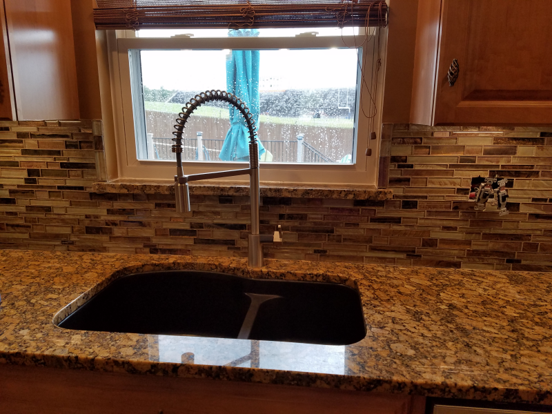 Kitchen sink with granite countertop, mosaic tile backsplash, and window with a view.
