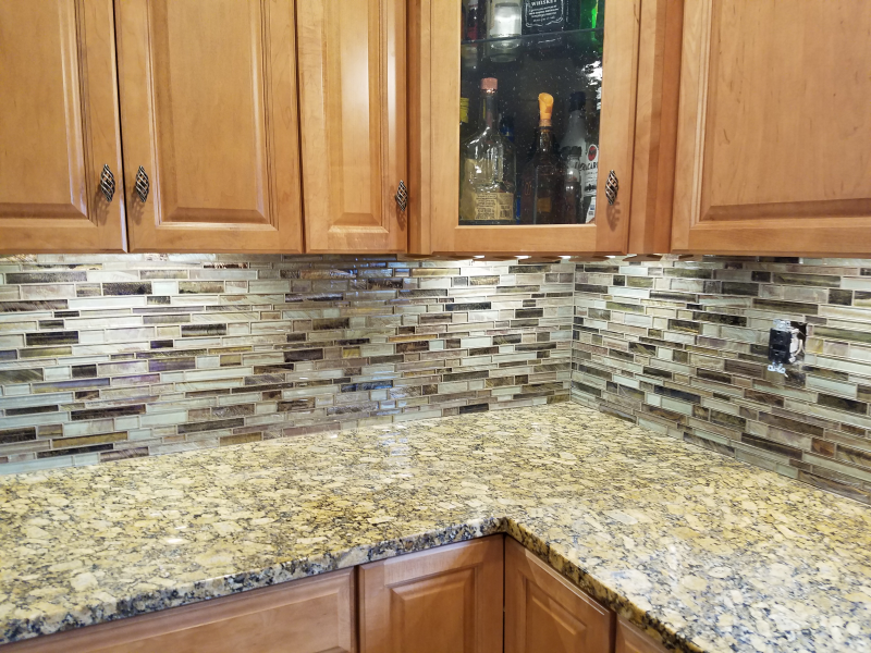 Kitchen corner with light brown cabinets, granite countertops, and mosaic backsplash.