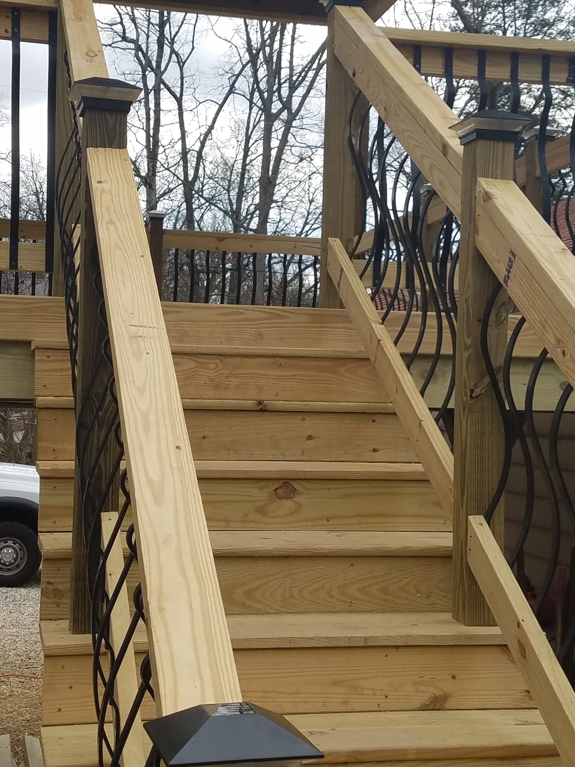 Wooden staircase leading up to a deck with black metal railing.