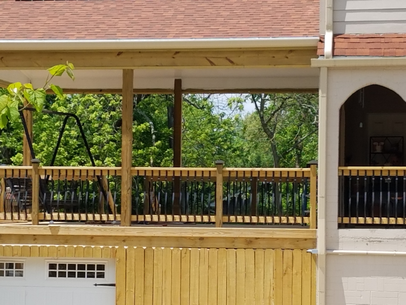 Wooden deck with black railings overlooking a green backyard, attached to a house with a garage.