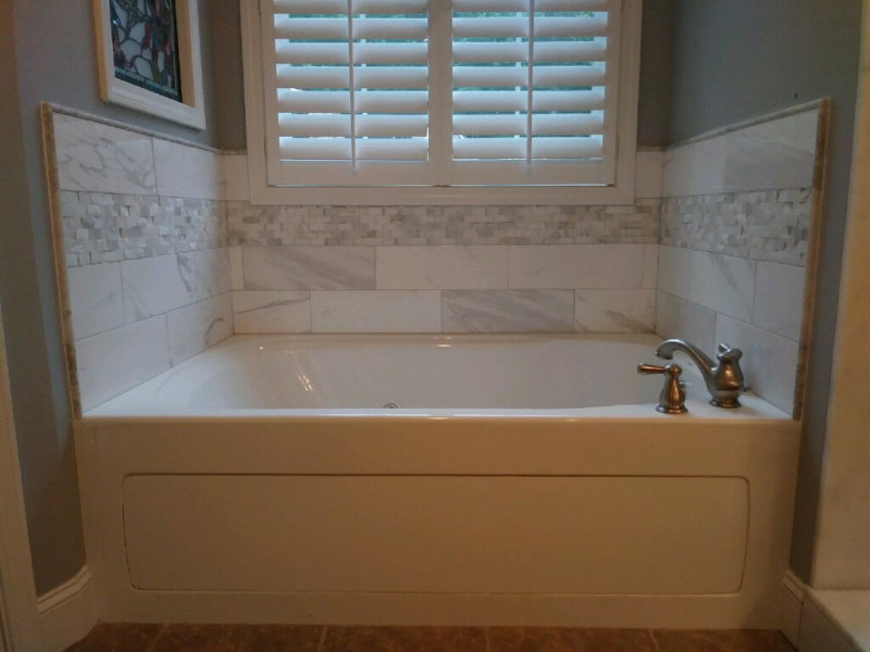 White bathtub with marble tile backsplash beneath a window with closed shutters.