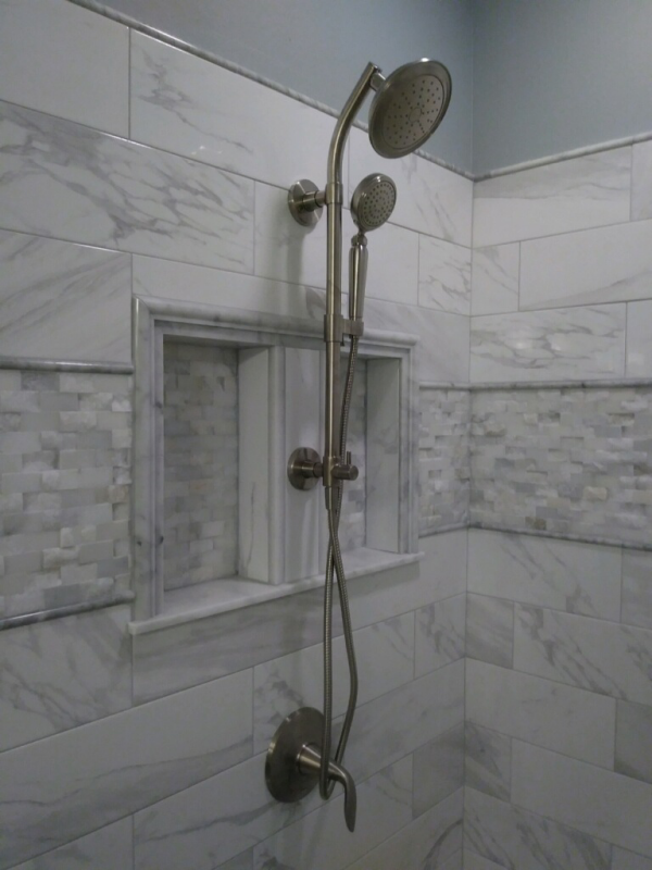 Shower with marble-look tile, niche, and dual showerheads in a corner setting.