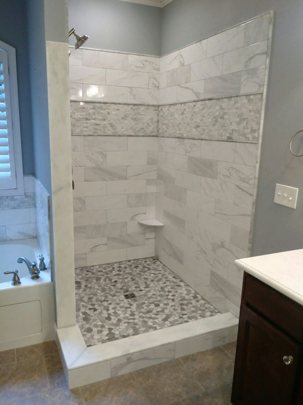Bathroom with tiled shower and pebble floor, white, gray, and brown tones.
