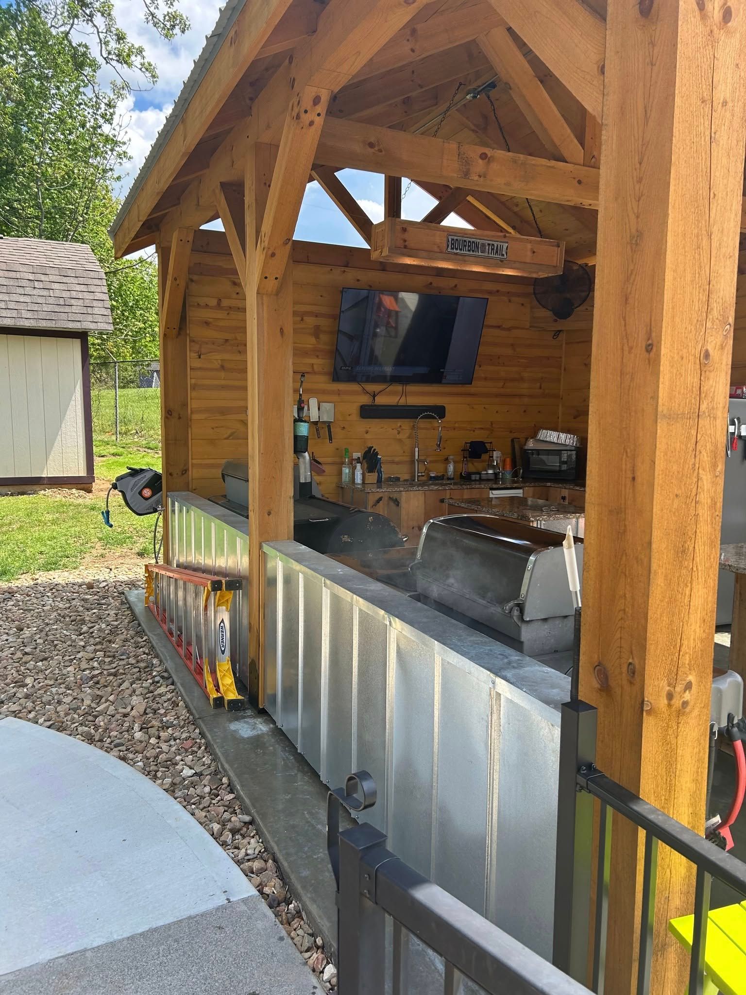 Wooden outdoor bar with a TV, metal countertop, and black railings.