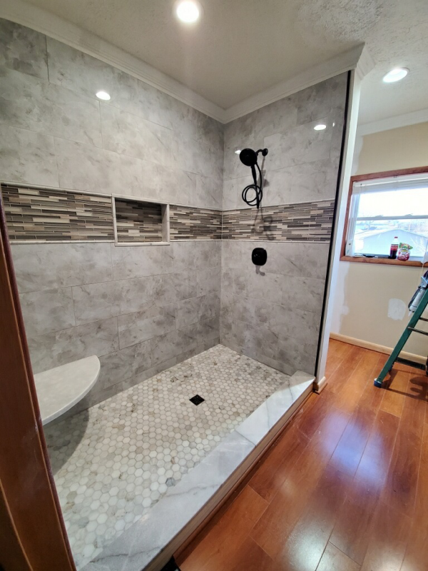 Newly tiled shower with gray walls, pebble floor, and glass door.