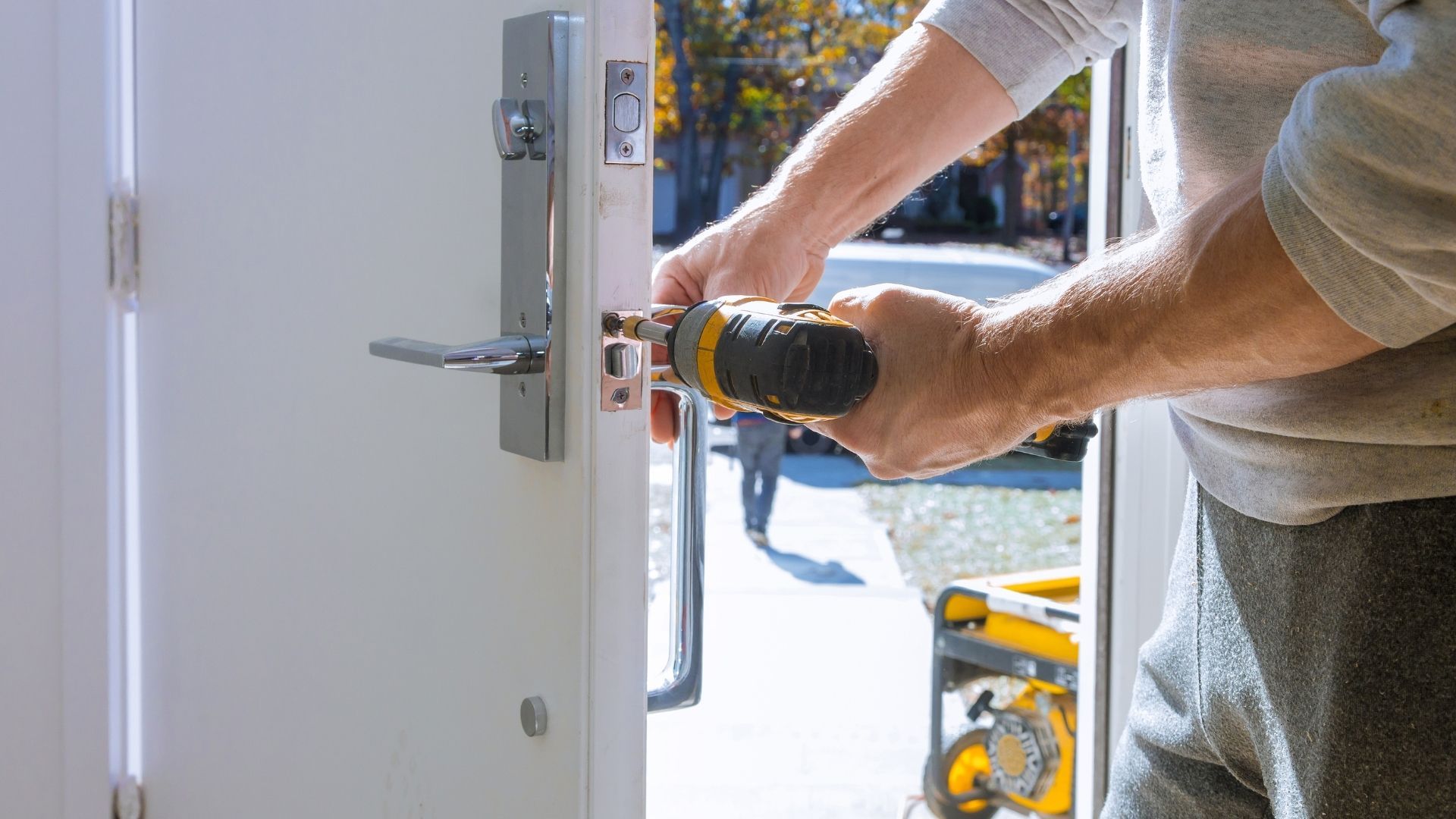 Person installing a door lock with a power drill outdoors.