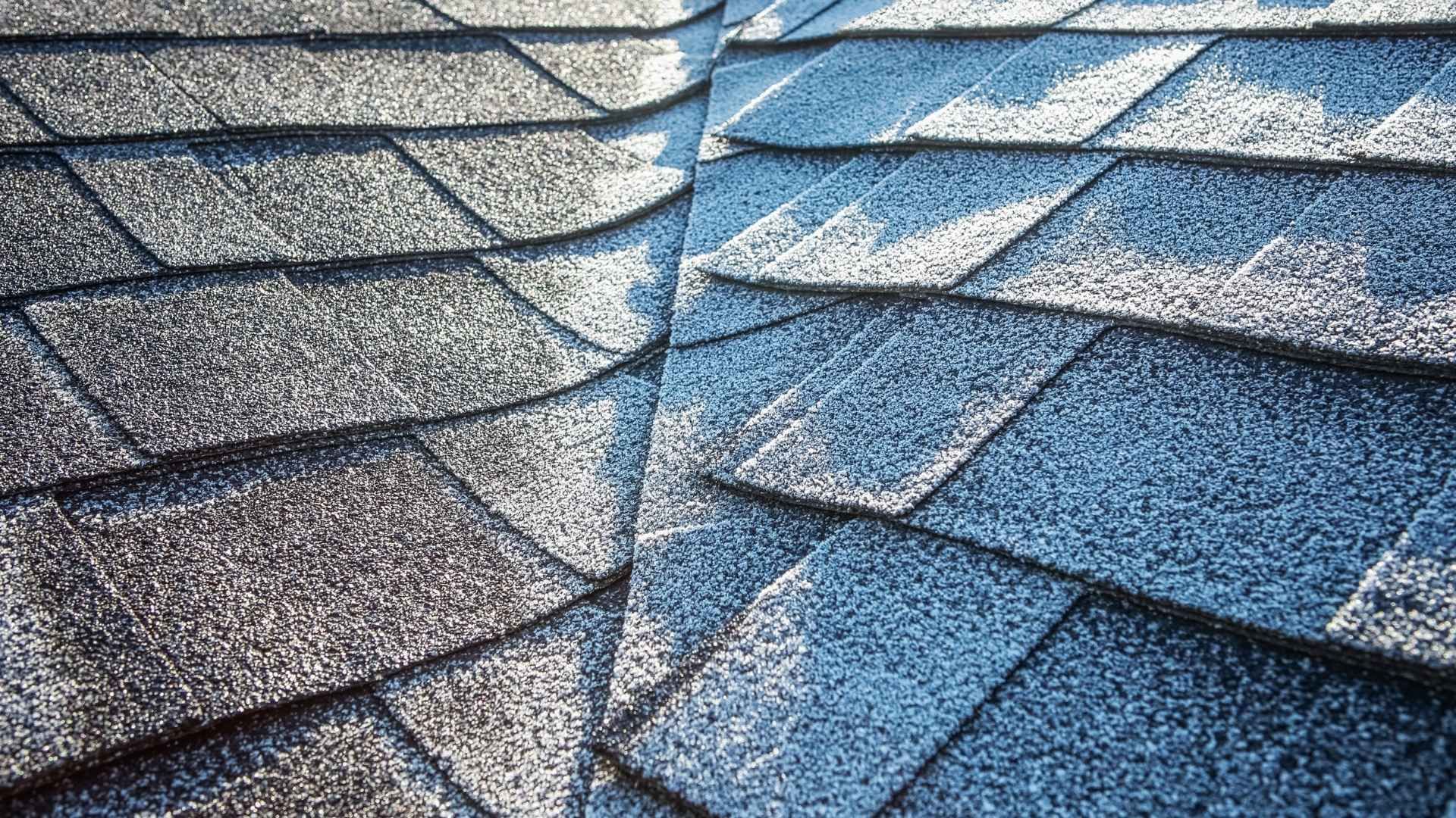 Close-up of asphalt shingle roof with a dark gray color on a bright sunny day.