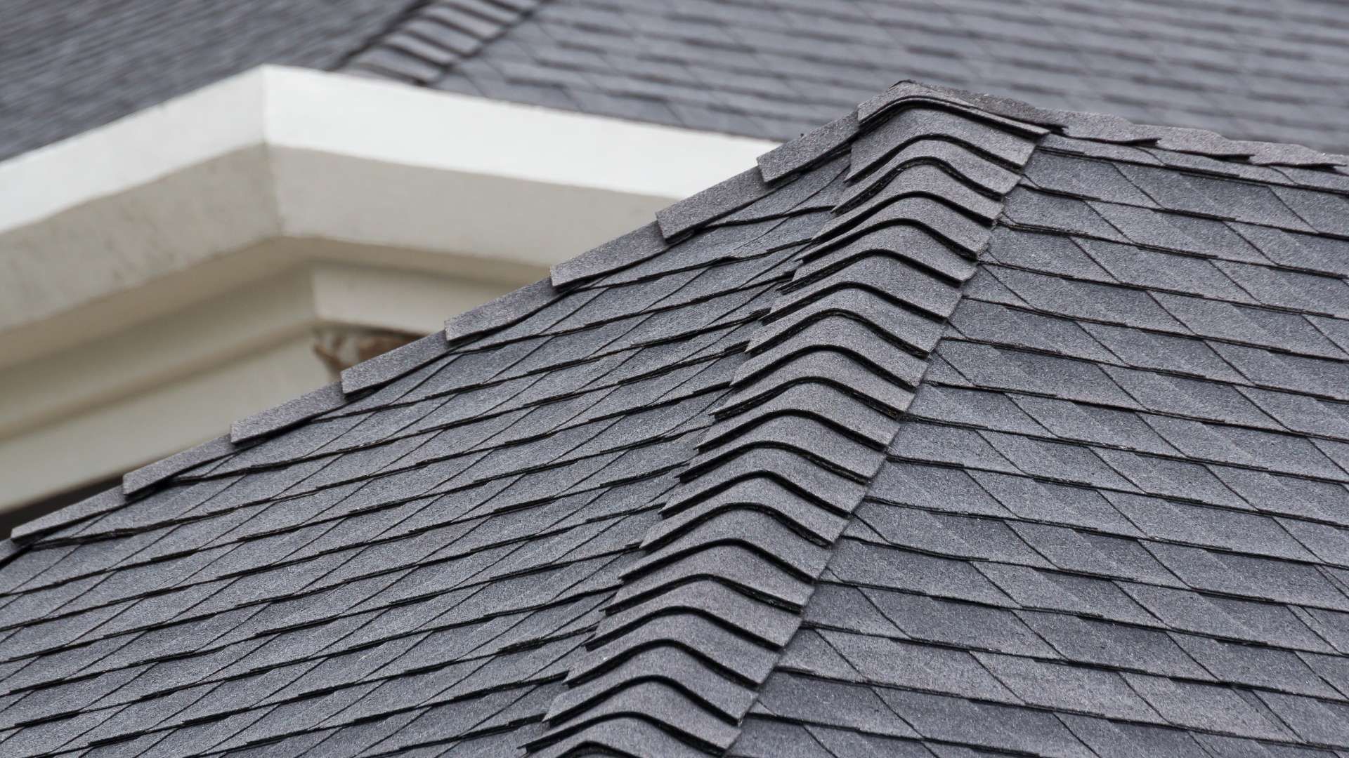 Dark gray asphalt shingle roof with a ridge, next to a white architectural feature.