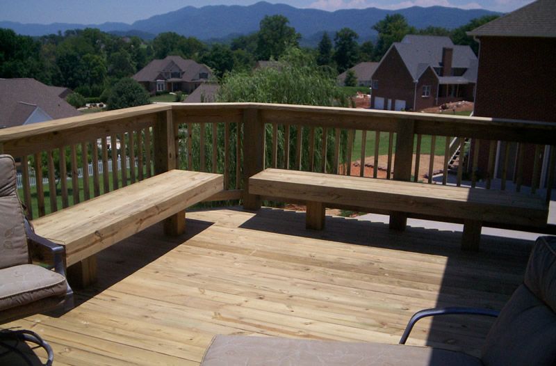 Wooden deck with built-in benches, railings, and mountain view in background on a sunny day.
