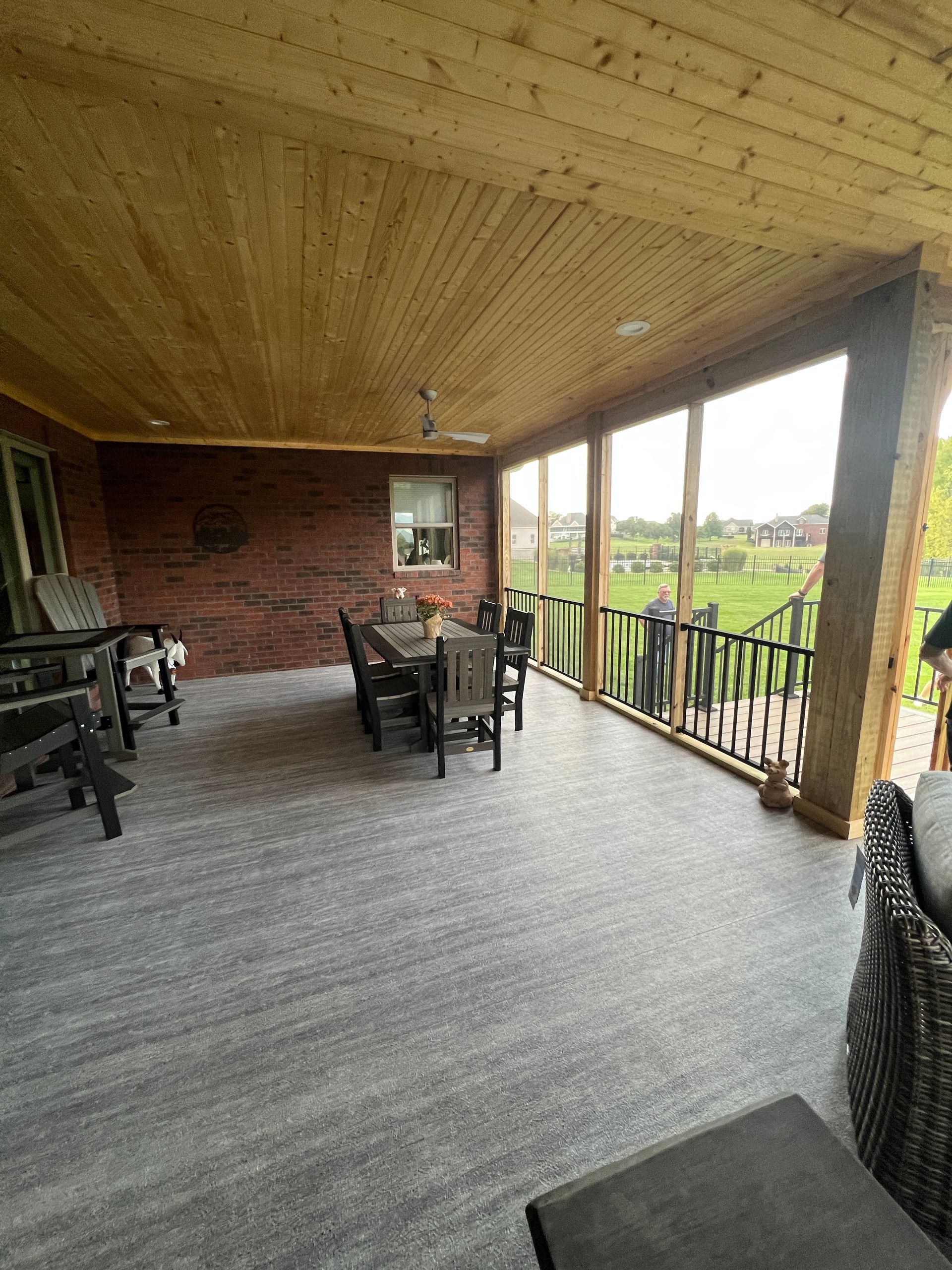 Covered outdoor patio with dining table and seating, overlooking a green landscape. 