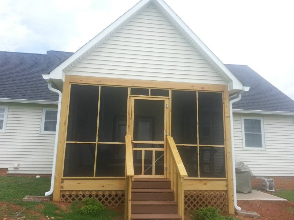 Screened porch with wooden frame, steps, and door attached to a light-colored house with white siding.