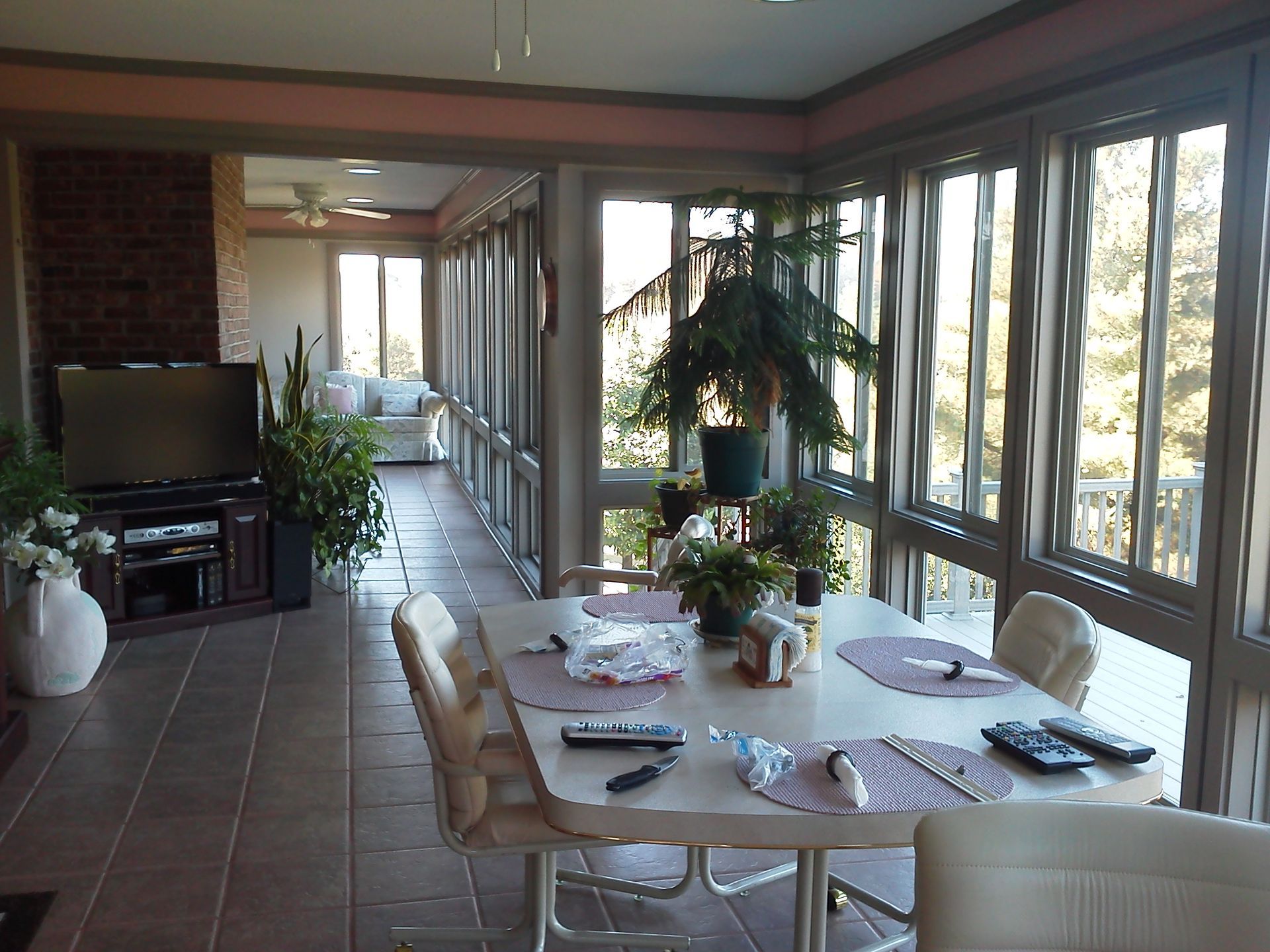 Sunroom with dining table, TV, and large windows overlooking a deck and trees.