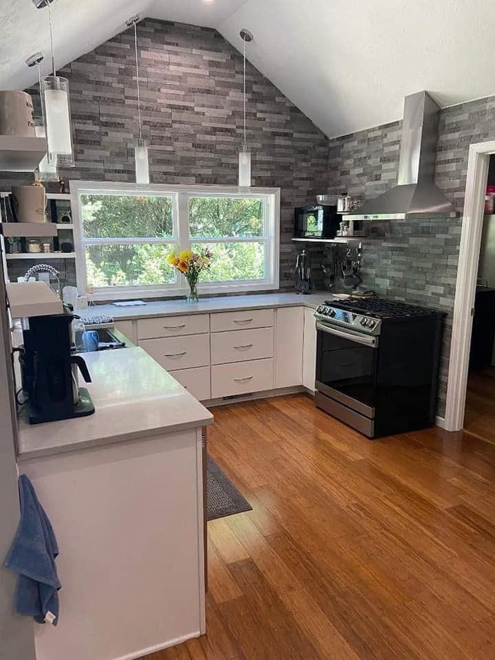 Modern kitchen with brick wall, white cabinets, stainless steel appliances, and wood flooring.