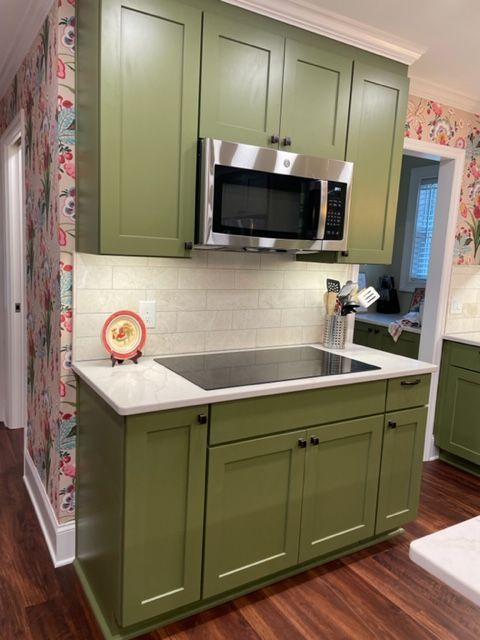 Green kitchen cabinets with stainless steel microwave above induction cooktop. Floral wallpaper.