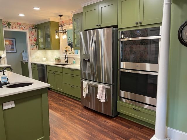 Green kitchen with stainless steel appliances, dark wood floors, and floral wallpaper.